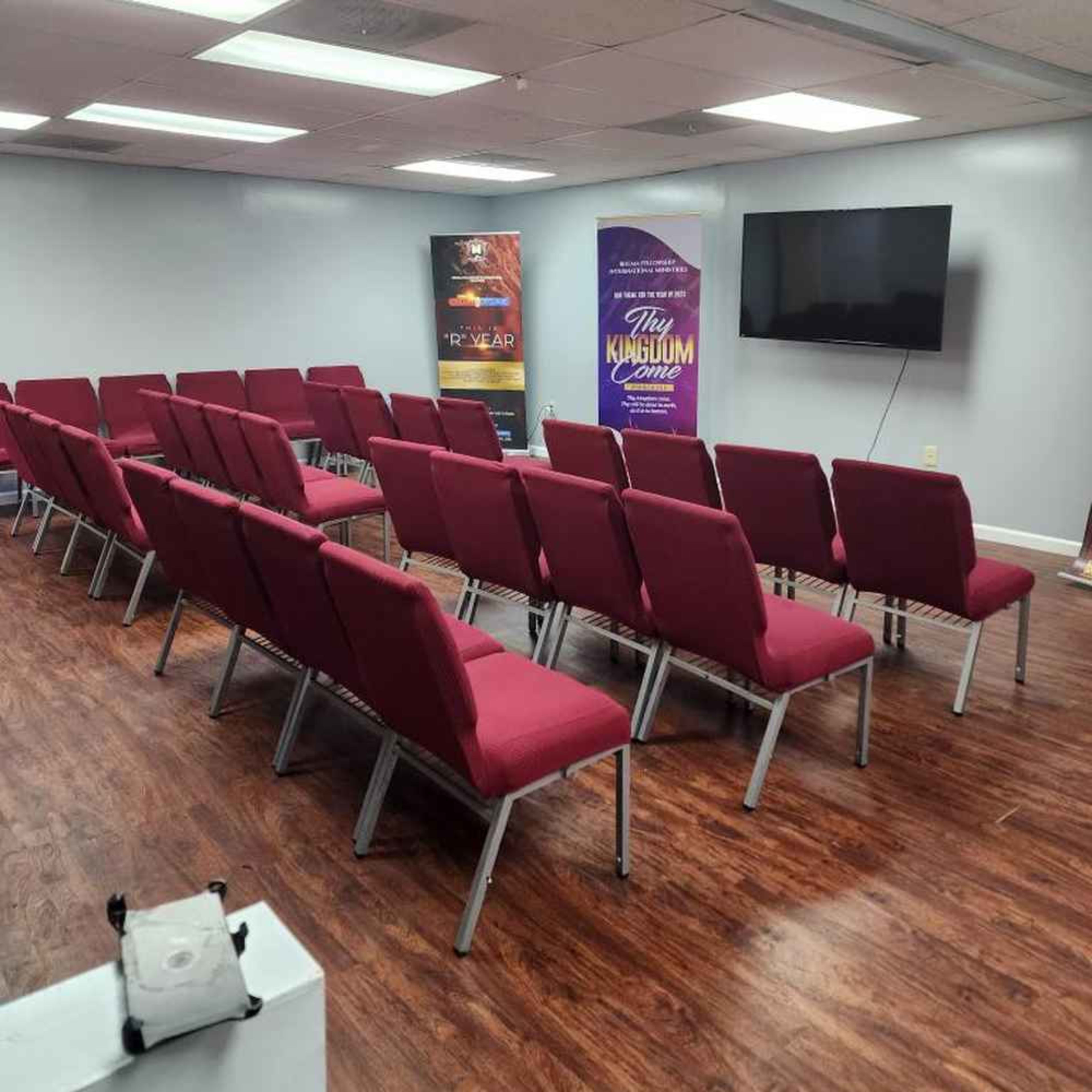 A room set up with red chairs arranged in rows facing a television screen and decorative banners on the walls.
