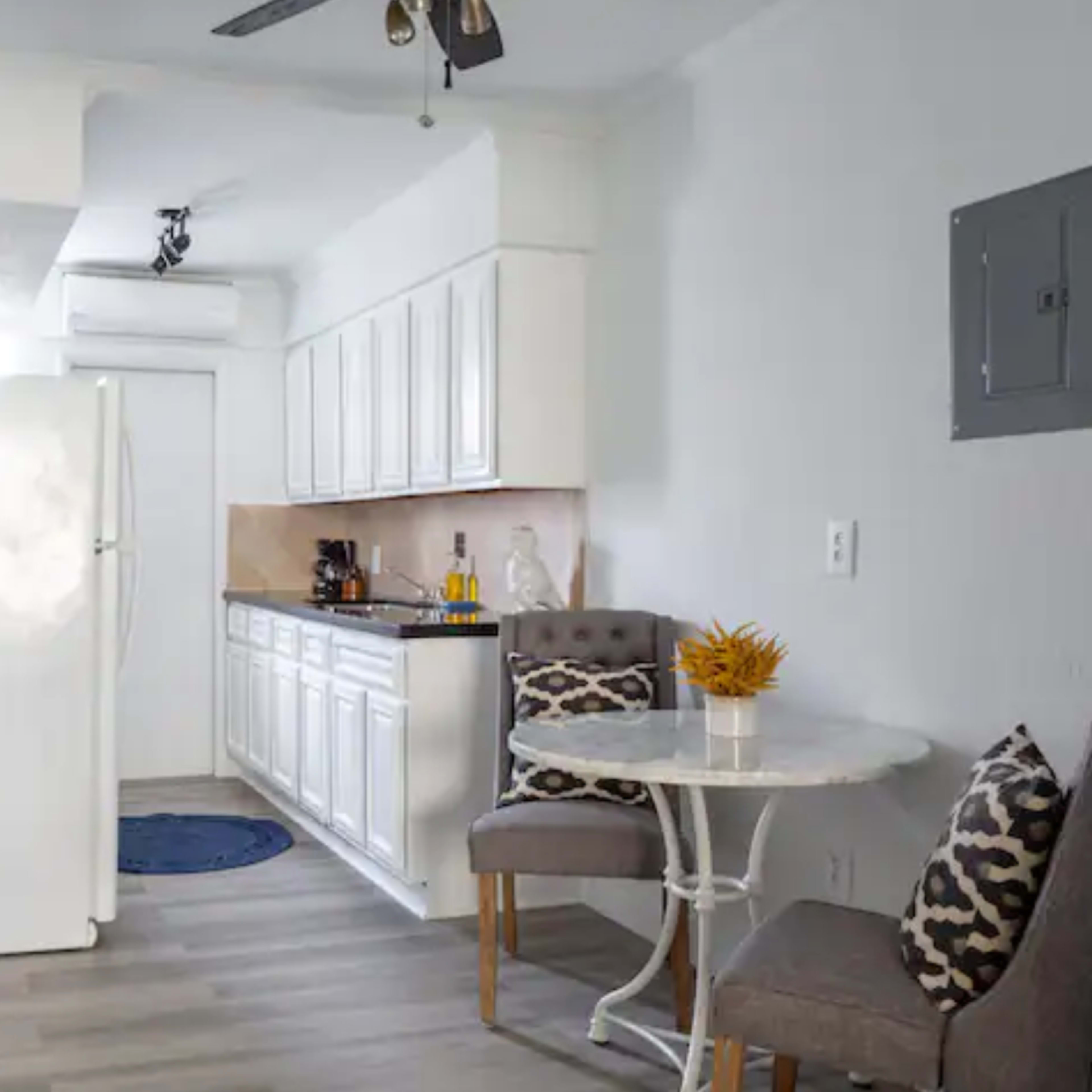 A kitchen space features white cabinetry, a round table with two chairs, and a refrigerator against a light gray wall.