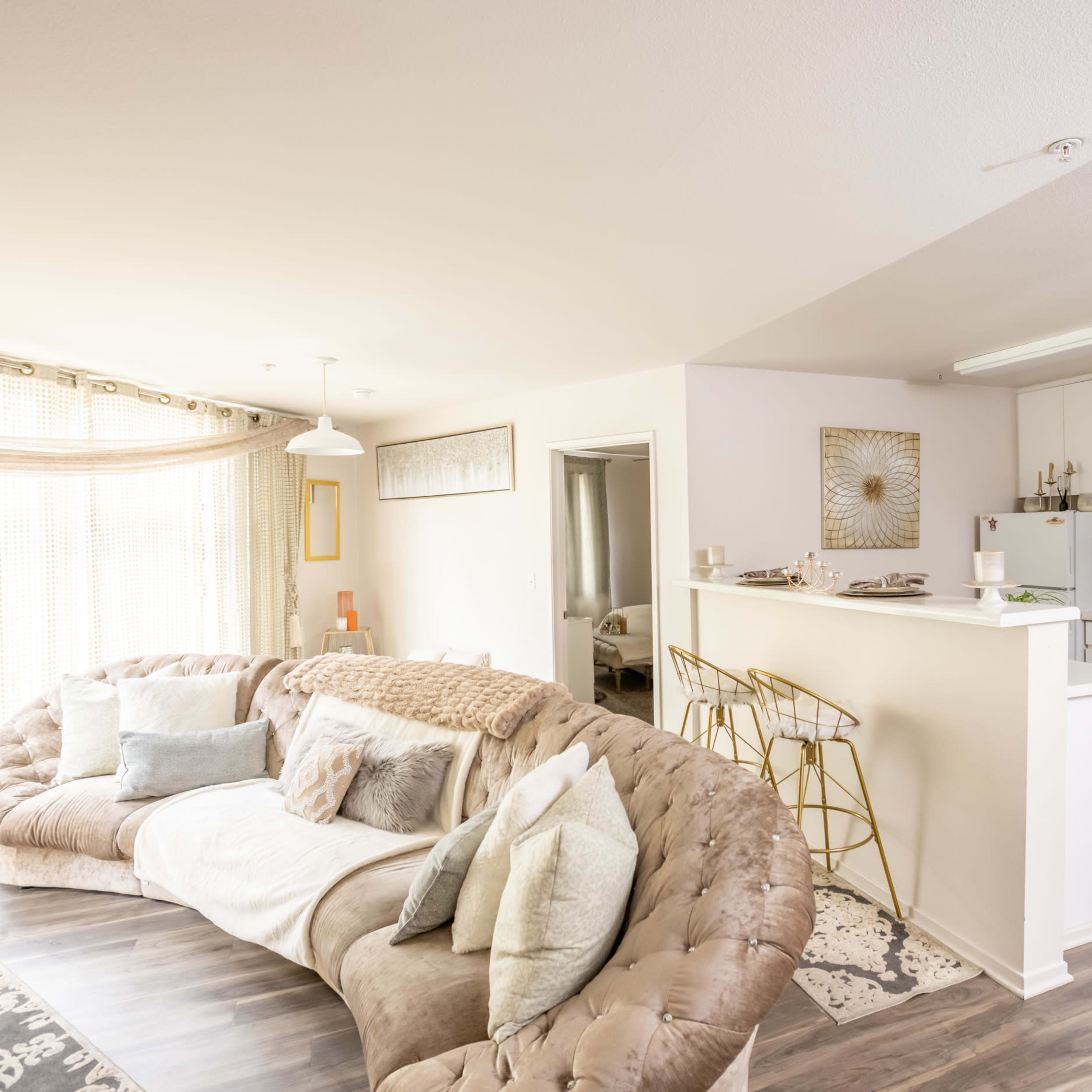 An open-concept living area and kitchen in a modern apartment, featuring a large sectional sofa and a breakfast bar with high stools.