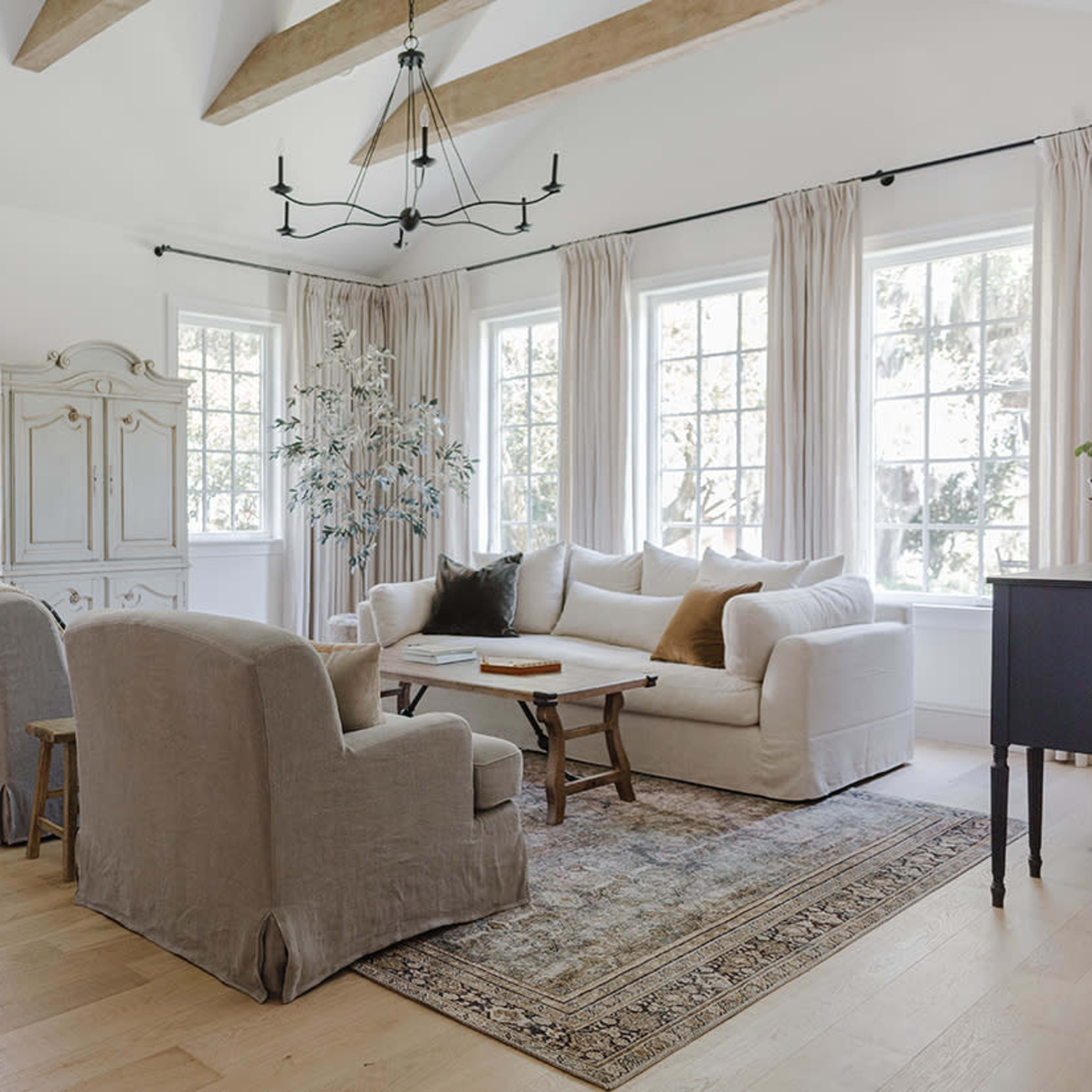 The living room features a light-colored sofa, two armchairs, a wooden coffee table, and large windows with long curtains.