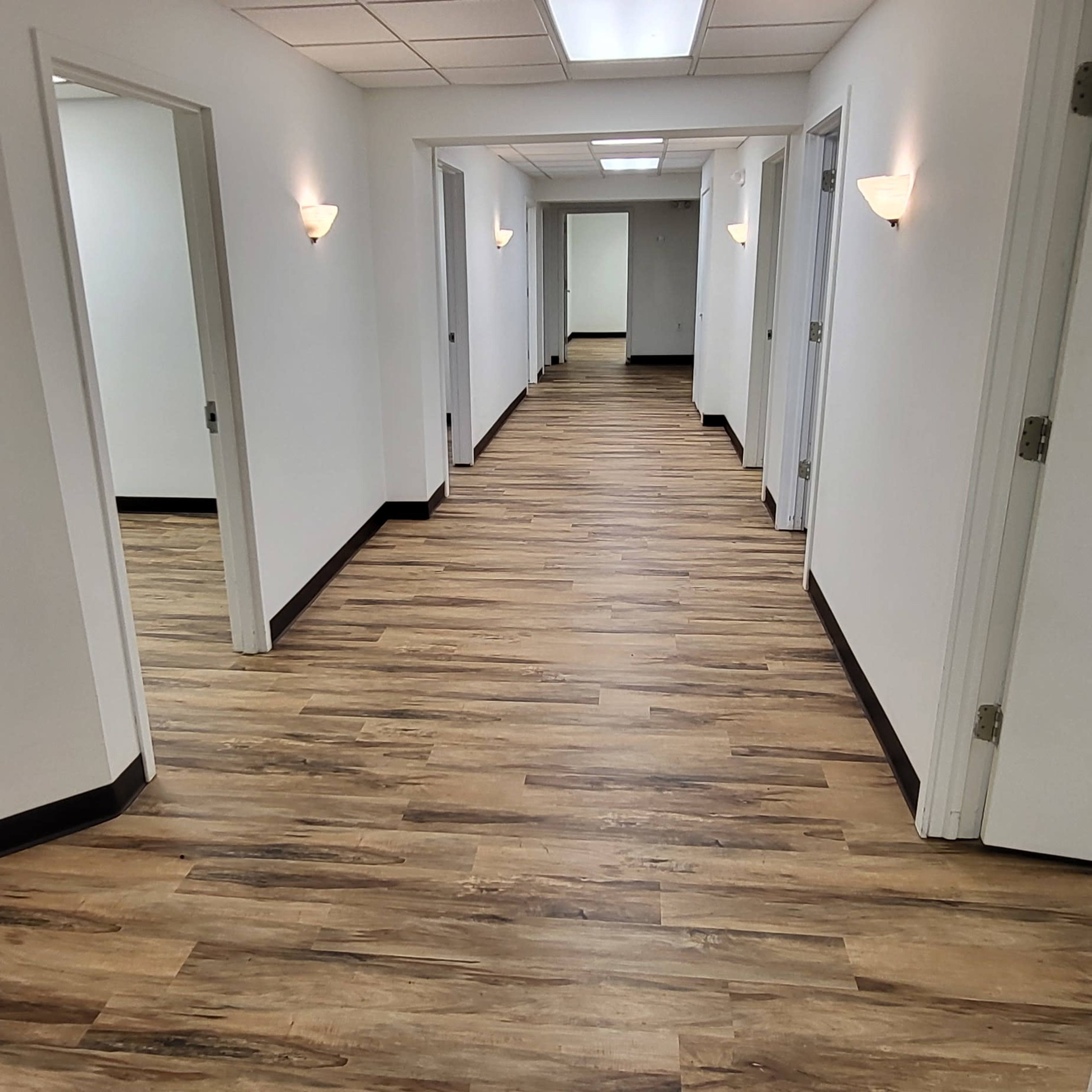 A long corridor with several doors on either side and wood-like flooring.