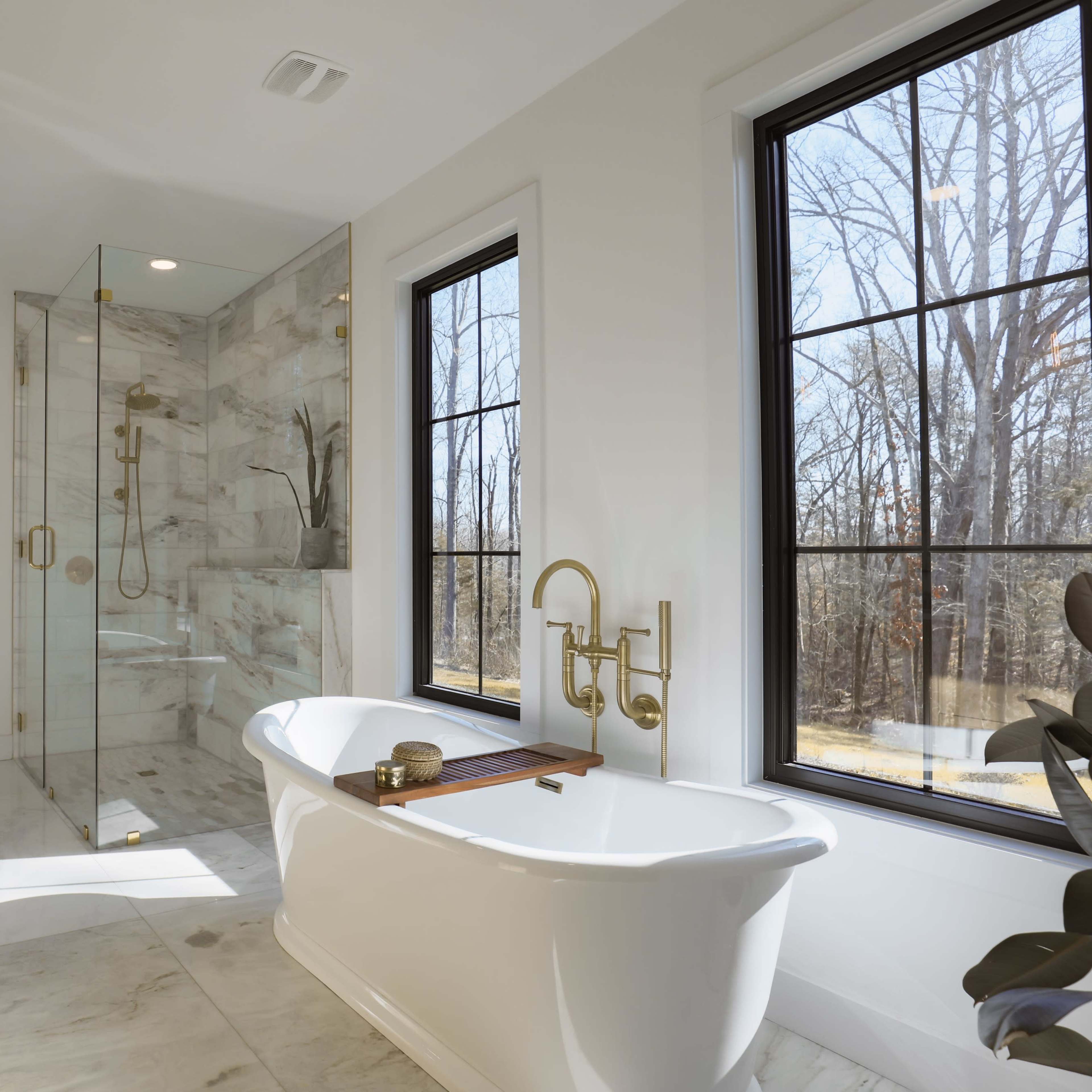 A modern bathroom featuring a freestanding bathtub, a glass shower enclosure, and large windows overlooking a wooded area.