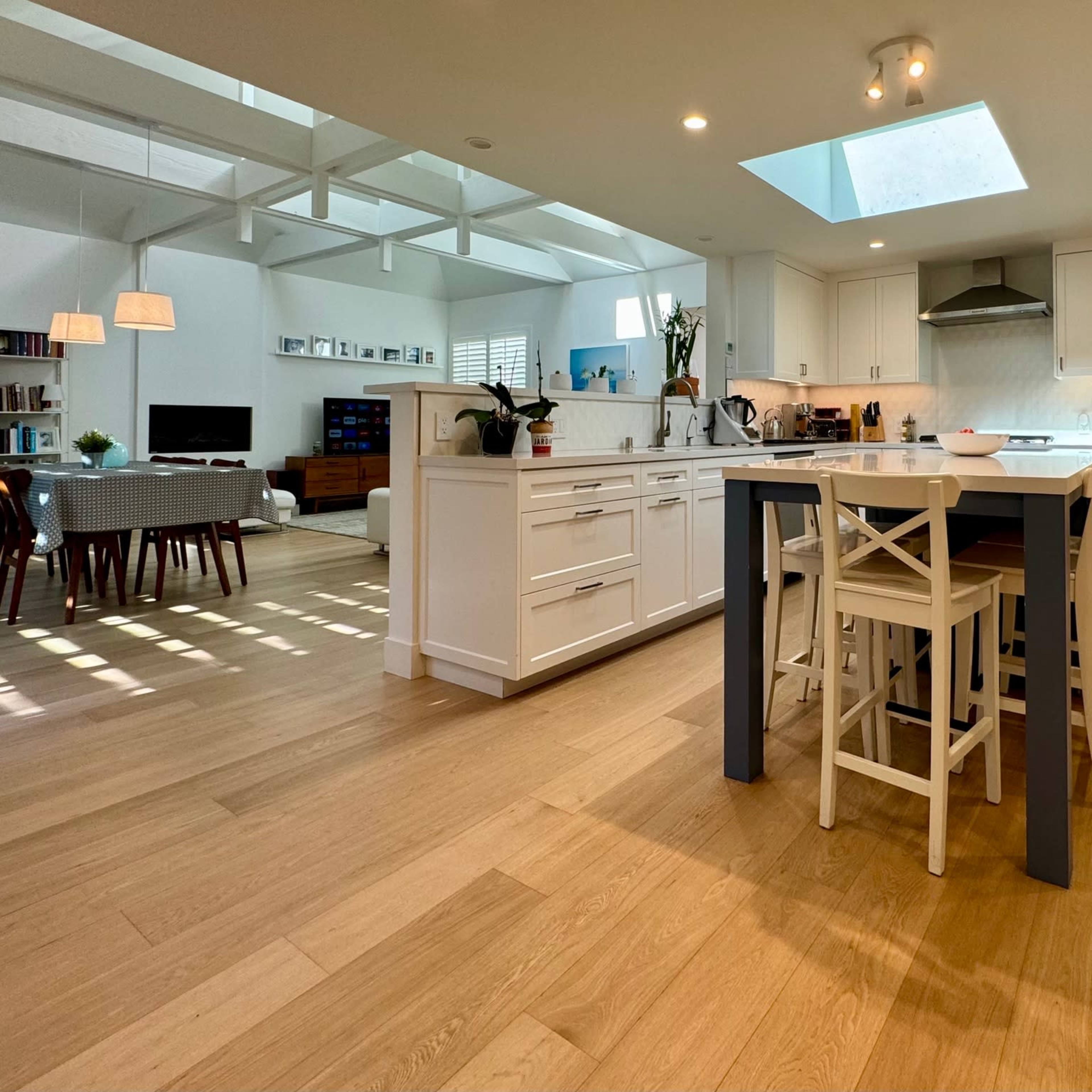 A bright, modern kitchen with white cabinetry, a central island with seating, and a skylight above, leading into a spacious living area.