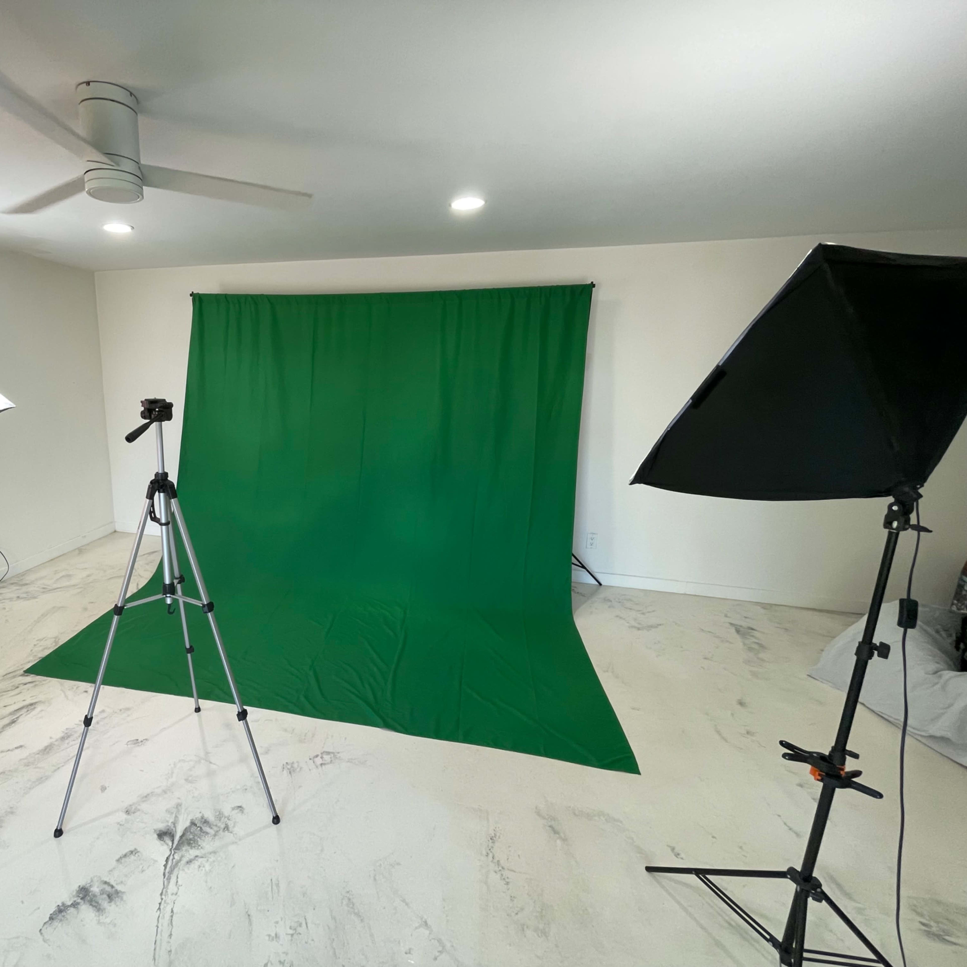 A photo studio setup with a green backdrop, lighting equipment, and a camera on a tripod.