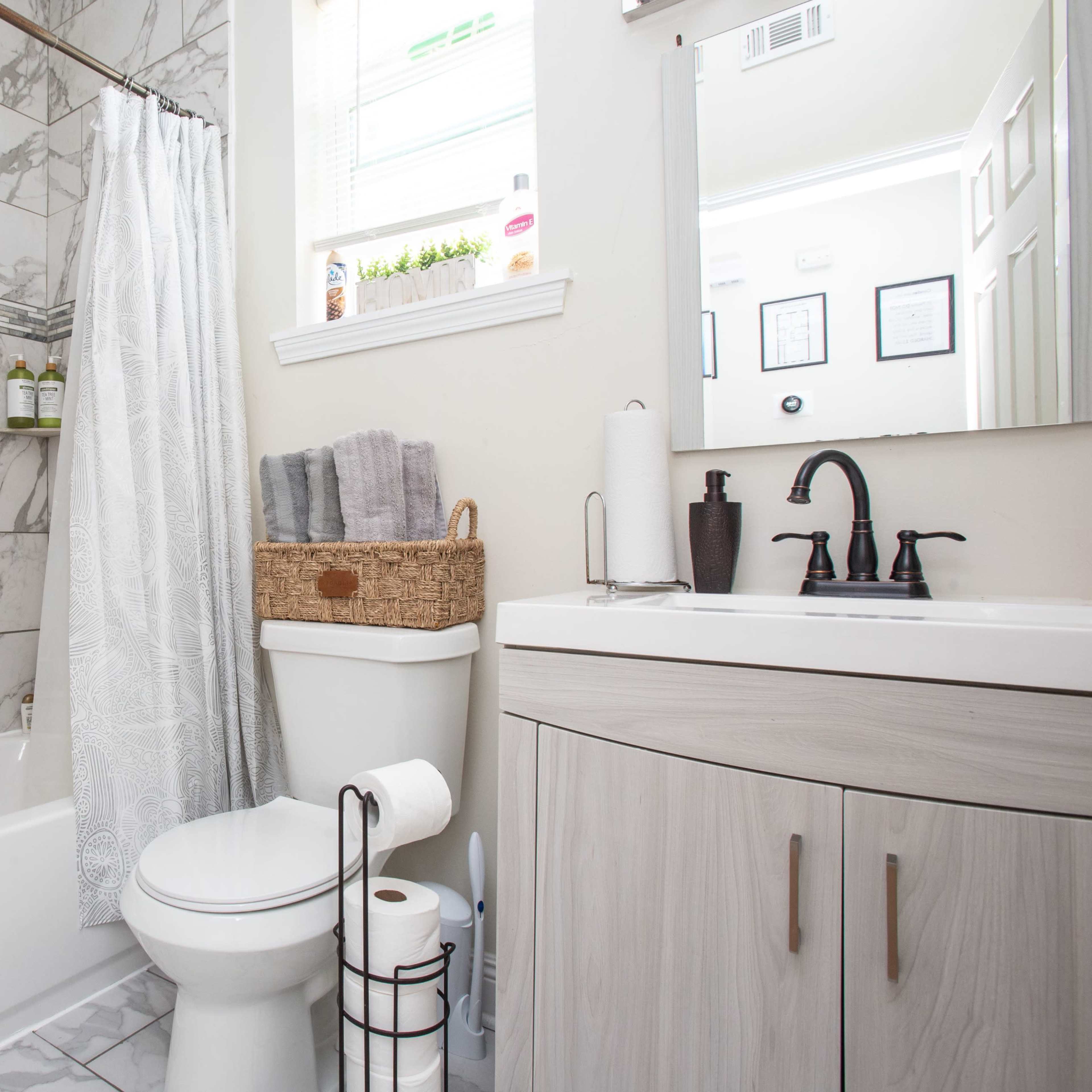 A modern bathroom features a tub with a marble-patterned wall, a decorative shower curtain, a vanity with a mirror, and neatly arranged toiletries.