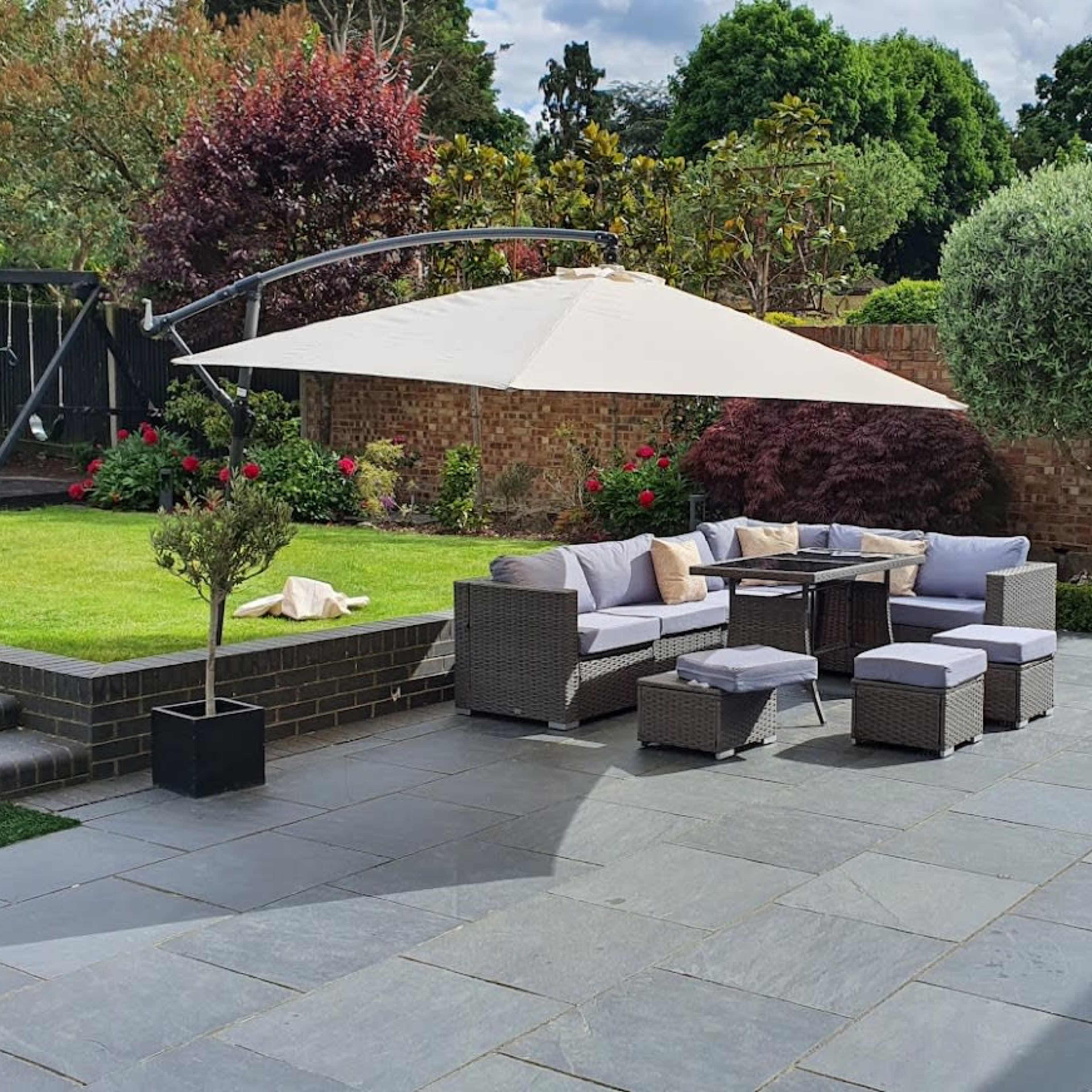 A landscaped garden with a patio area featuring outdoor furniture arranged under a large umbrella.