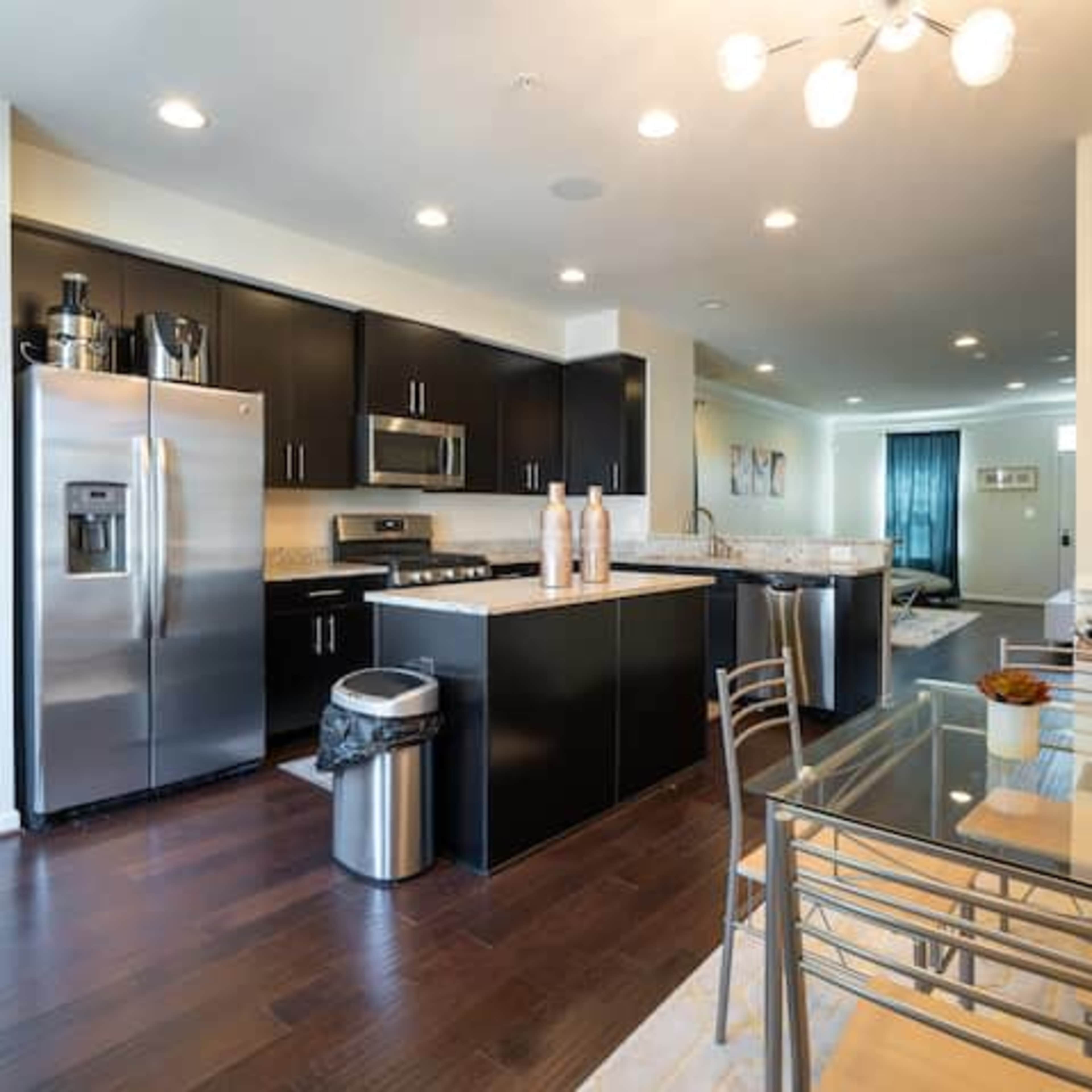 The kitchen features dark cabinetry, stainless steel appliances, and a central island with a dining area adjacent to it.
