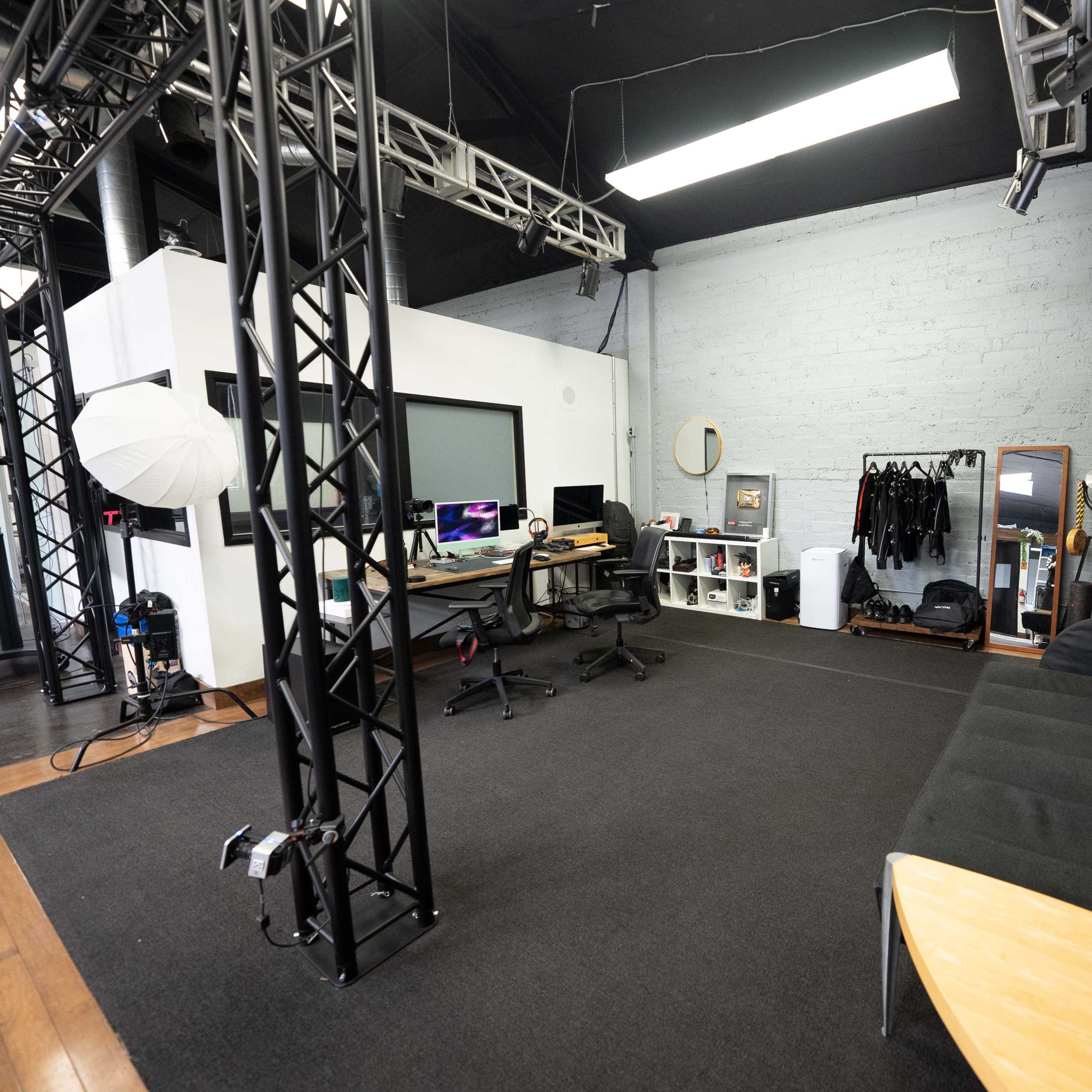 A modern studio space featuring a black carpet, a sectional couch, workstations with computers, and various studio equipment.