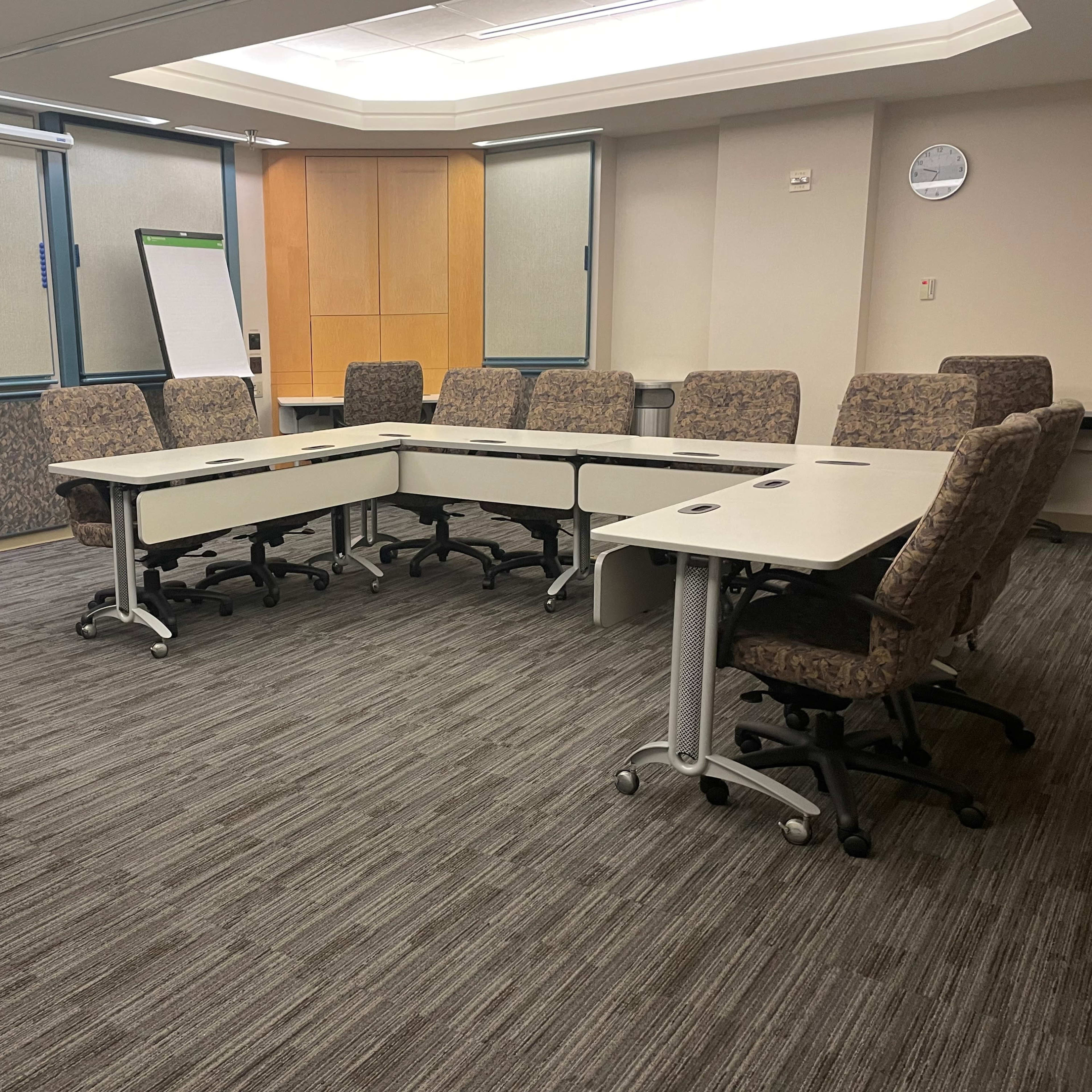 A conference room is set up with a large, oval table surrounded by eight chairs, with a television and a whiteboard positioned at one end.