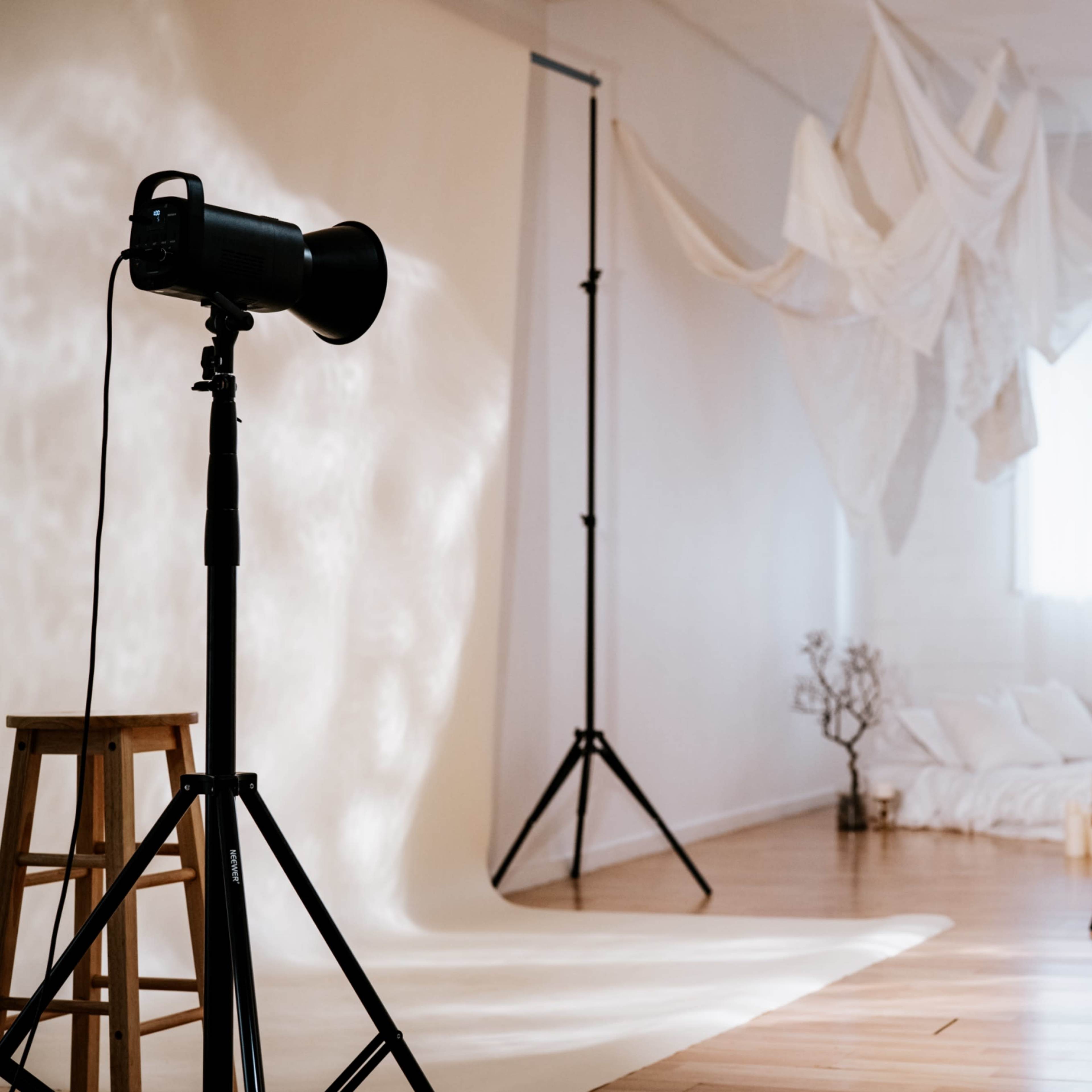A photography studio is set up with a spotlight, backdrops, and a minimalist bed arrangement in the background.