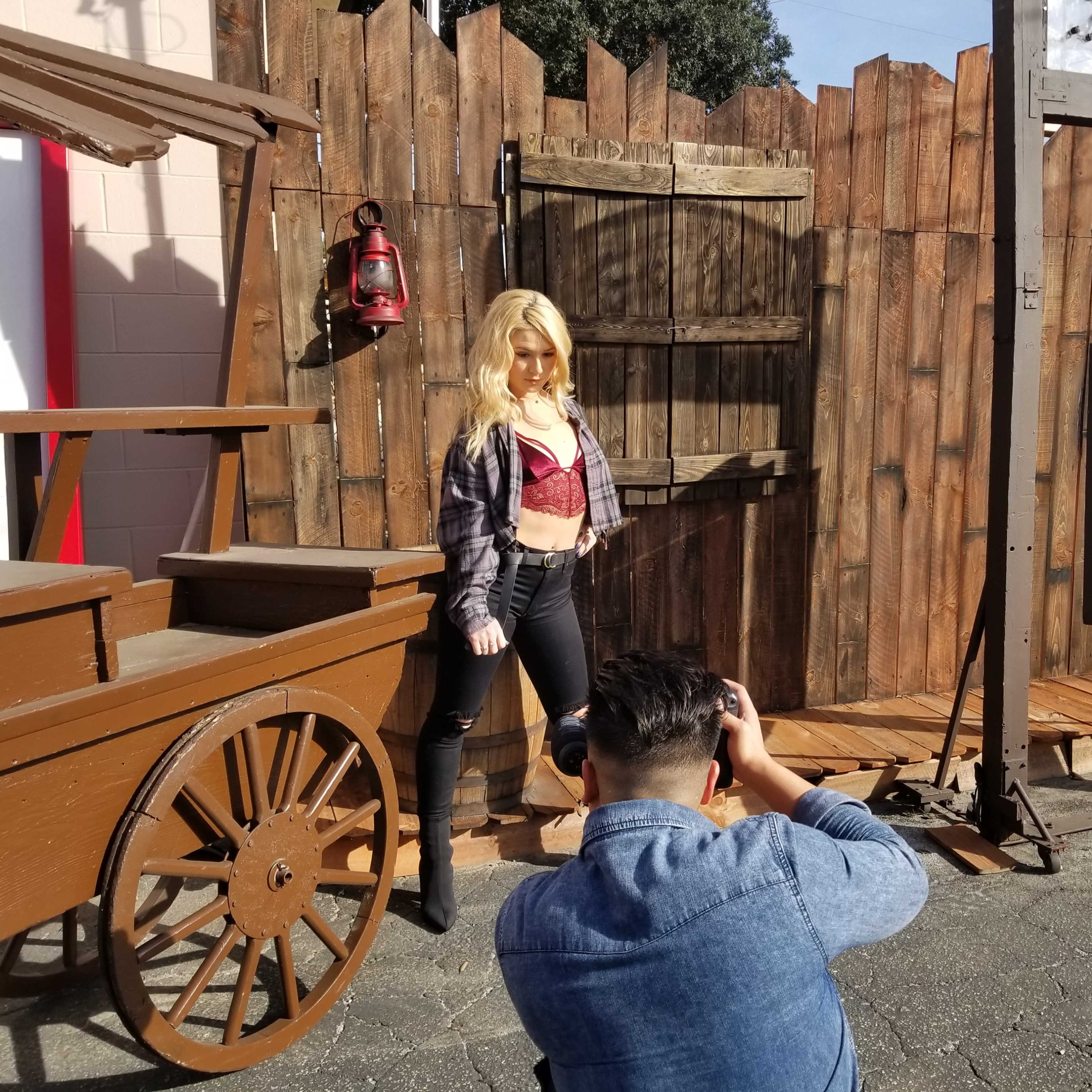 A model poses in front of a rustic wooden backdrop while a photographer captures the shot.