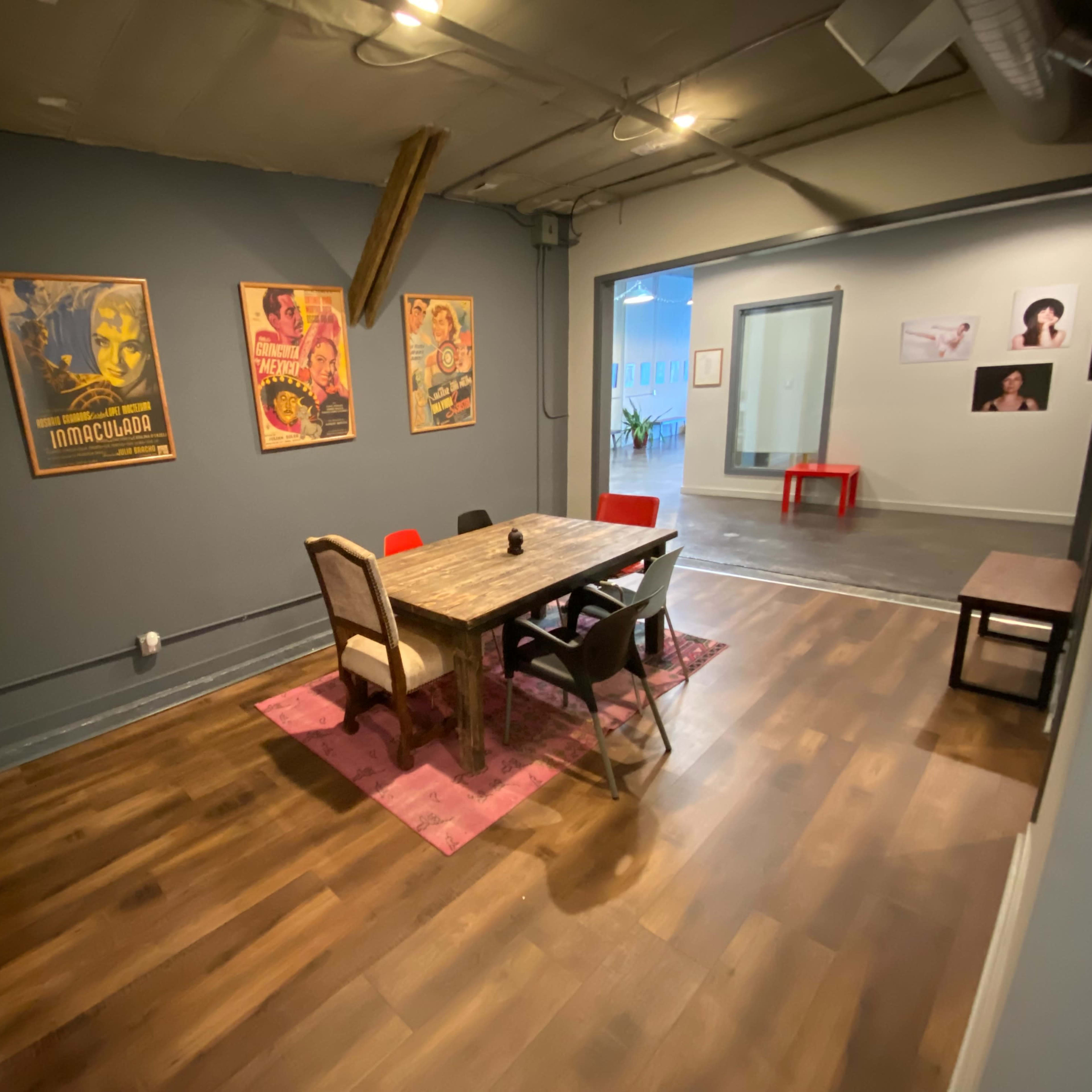 A cozy meeting room with a large wooden table, surrounded by chairs, and framed posters on the walls.