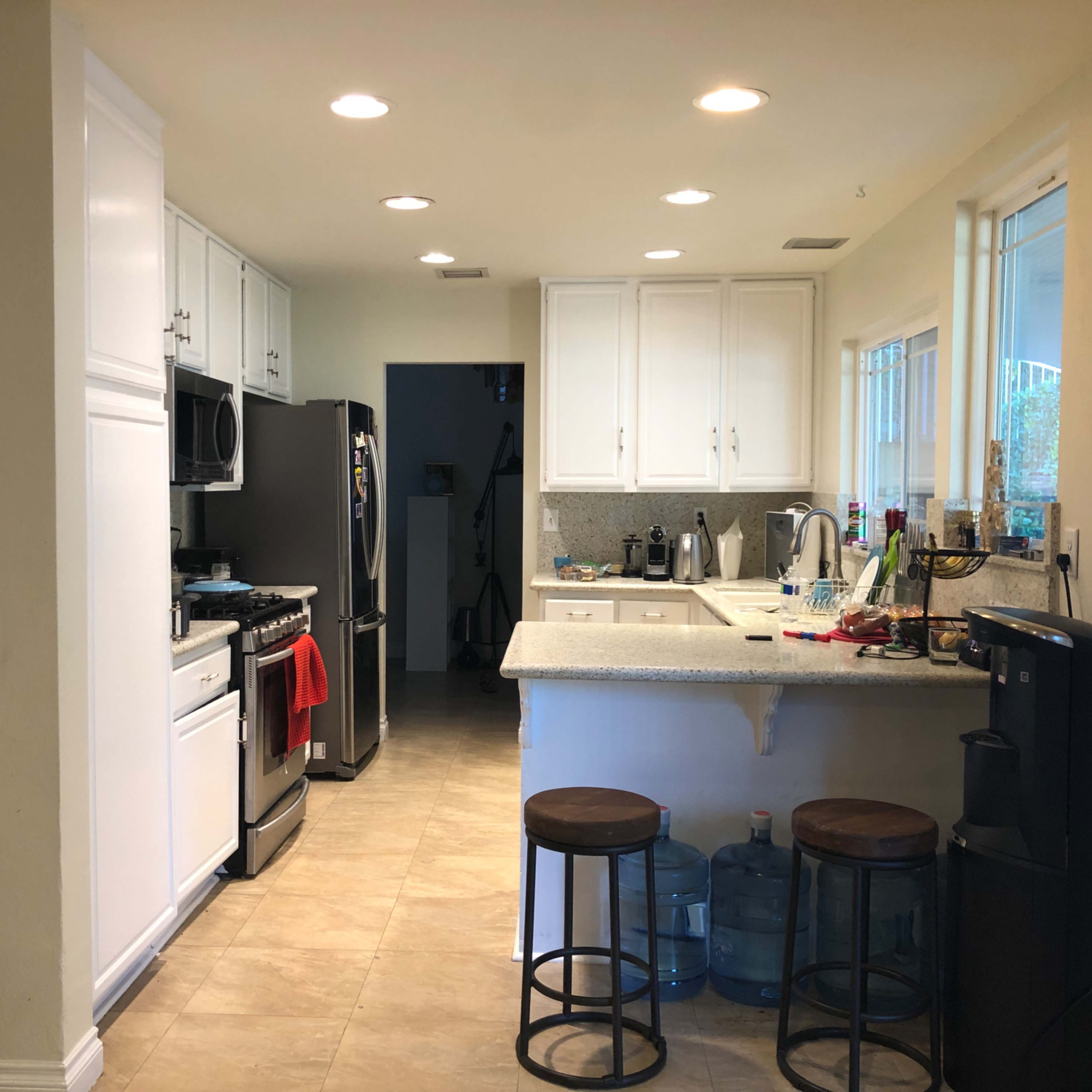 A bright kitchen features white cabinetry, stainless steel appliances, a counter with stools, and a water cooler near the entrance.