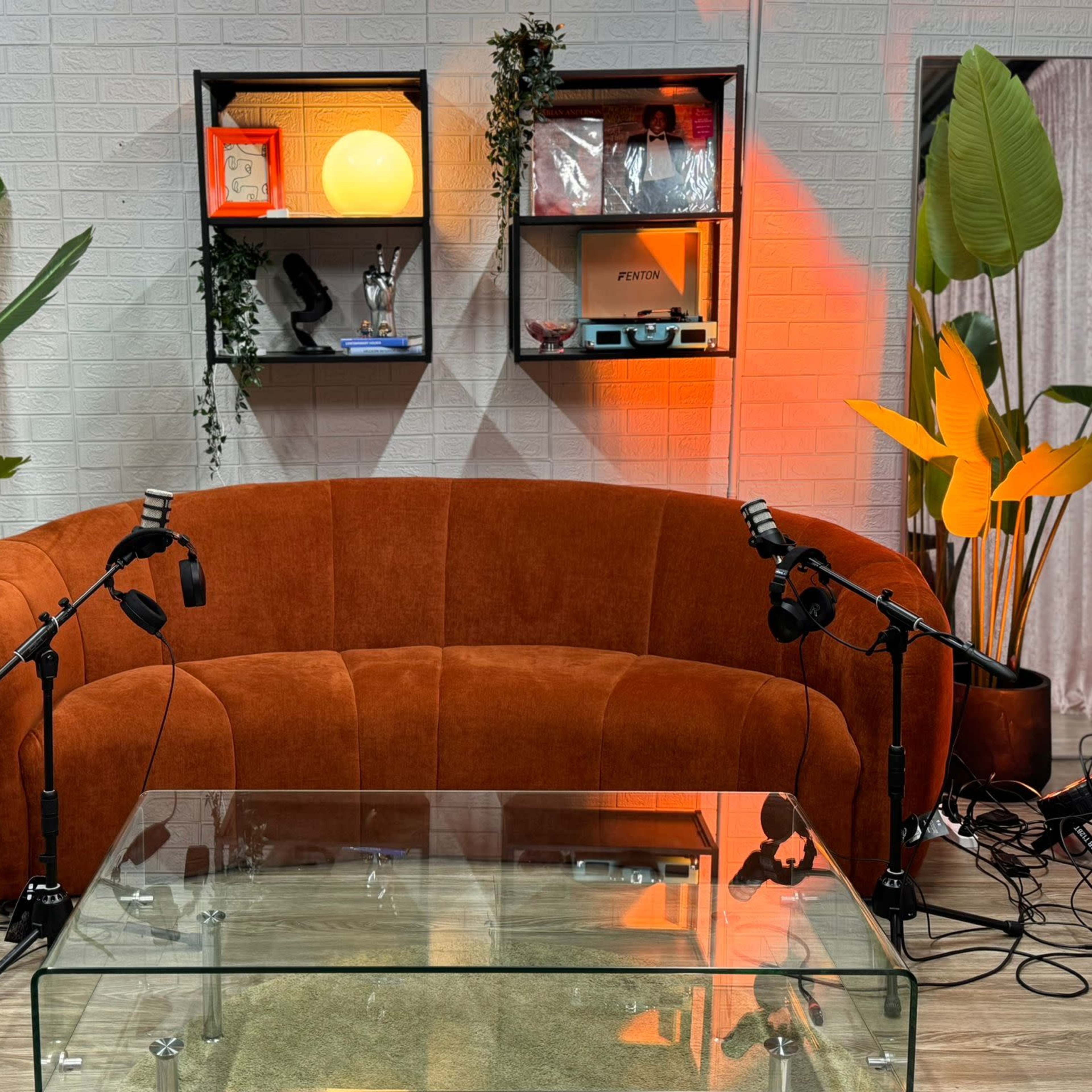 An orange curved sofa in a room with shelves, potted plants, and a glass coffee table.