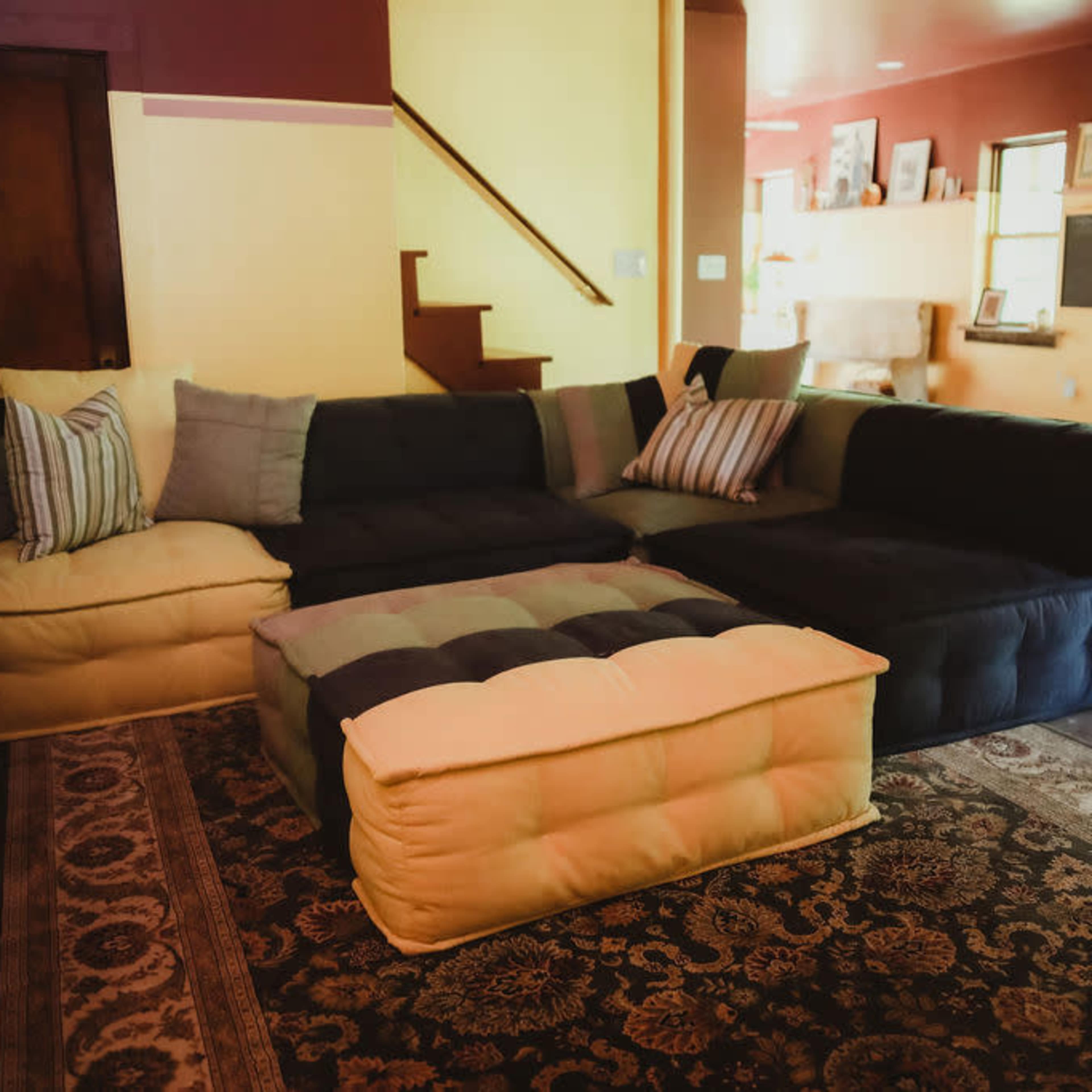 A large, modular couch in a cozy living space with a patterned rug and a staircase in the background.