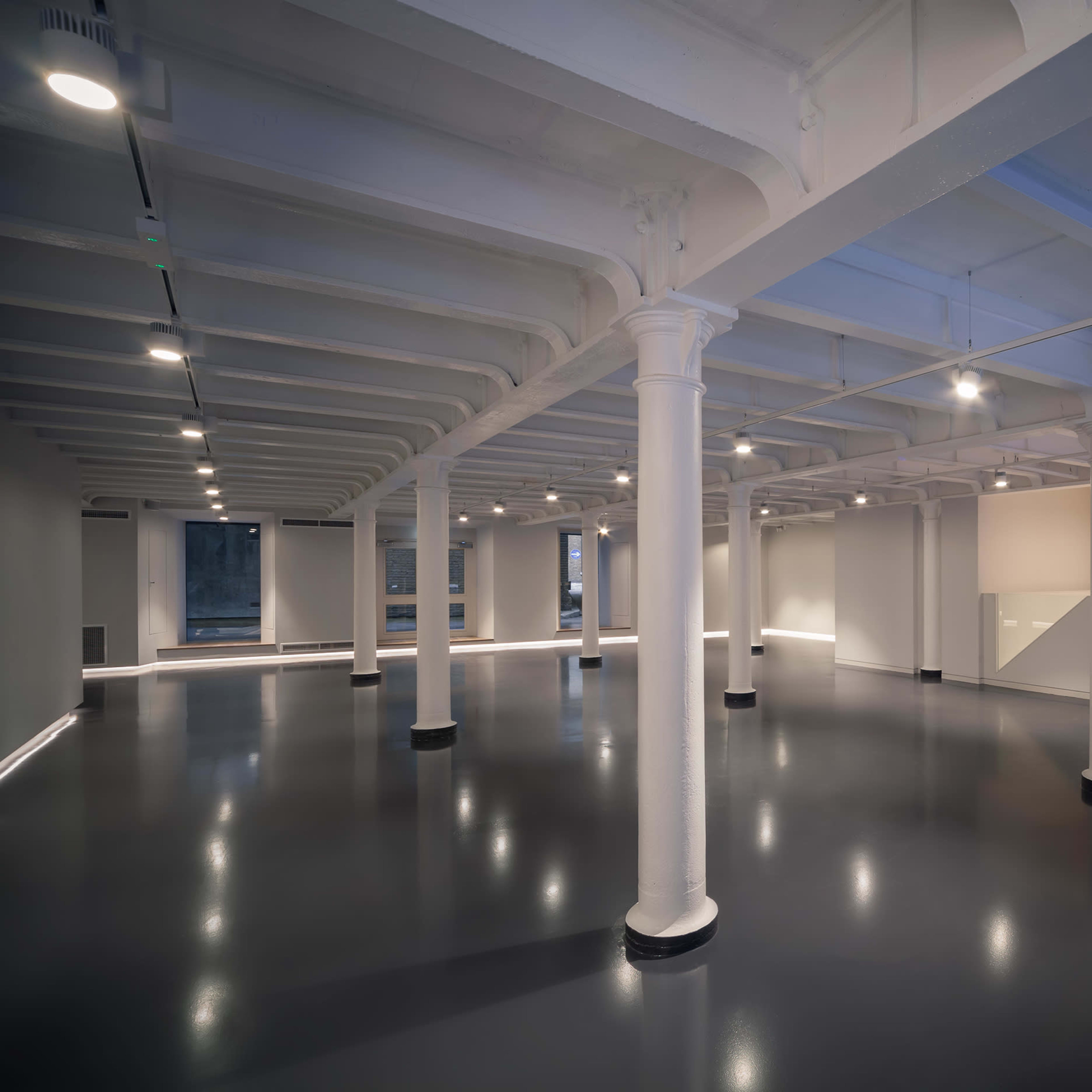 A spacious, modern interior featuring high ceilings, exposed beams, and polished flooring, illuminated by overhead lights.