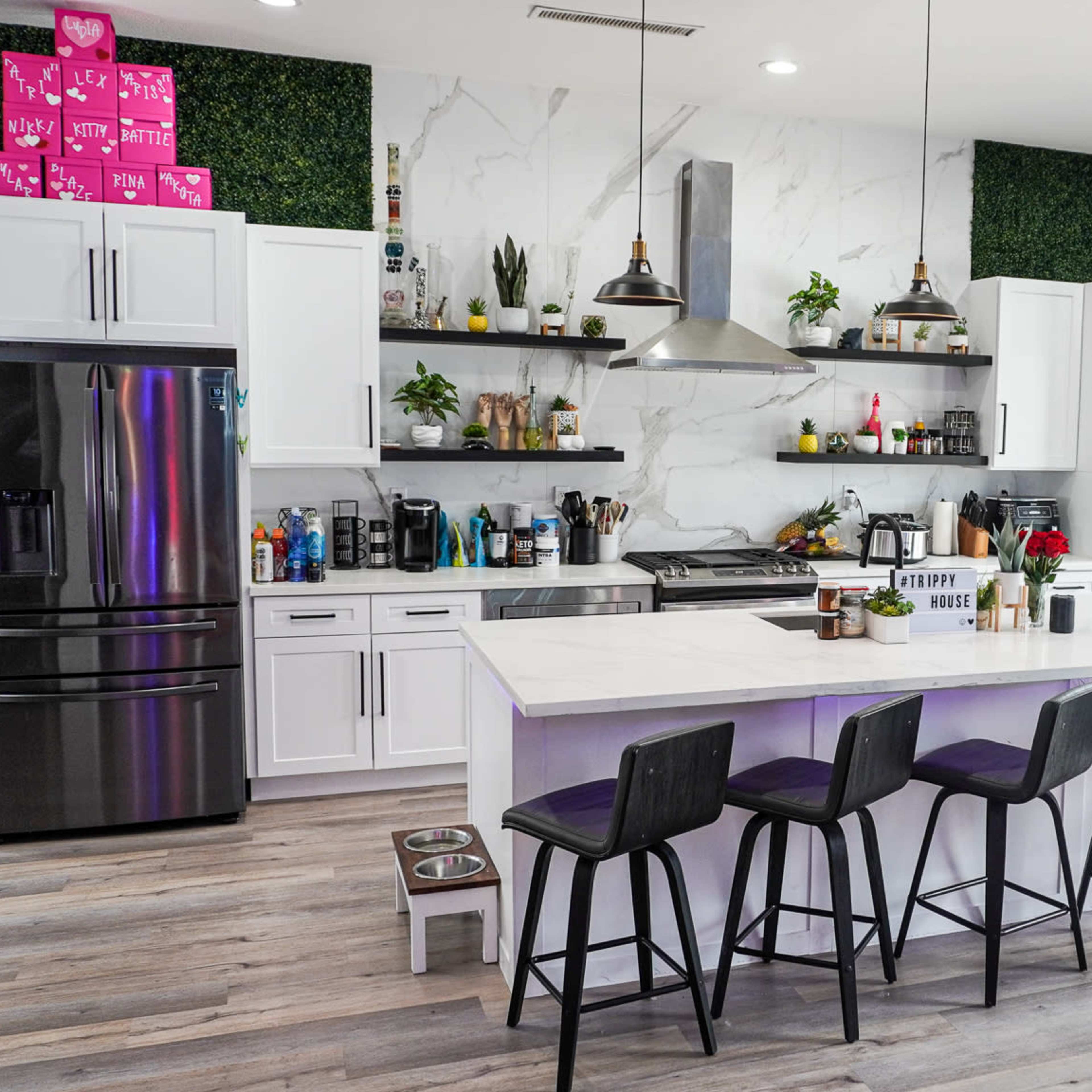 A modern kitchen with white cabinets, a large island with seating, and a decorative green wall featuring various plants.