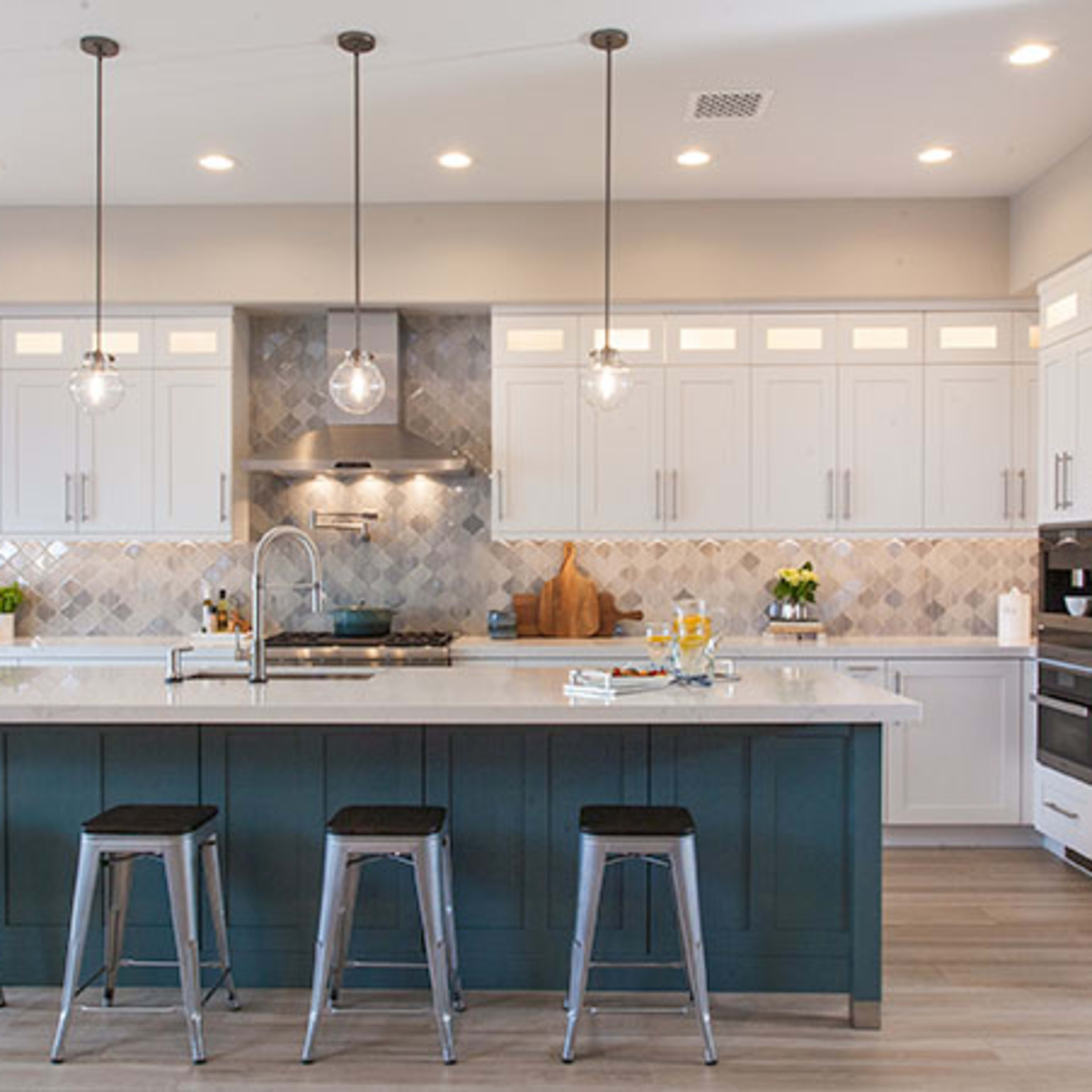 A modern kitchen with white cabinets, a gray tile backsplash, and a large island with bar stools.