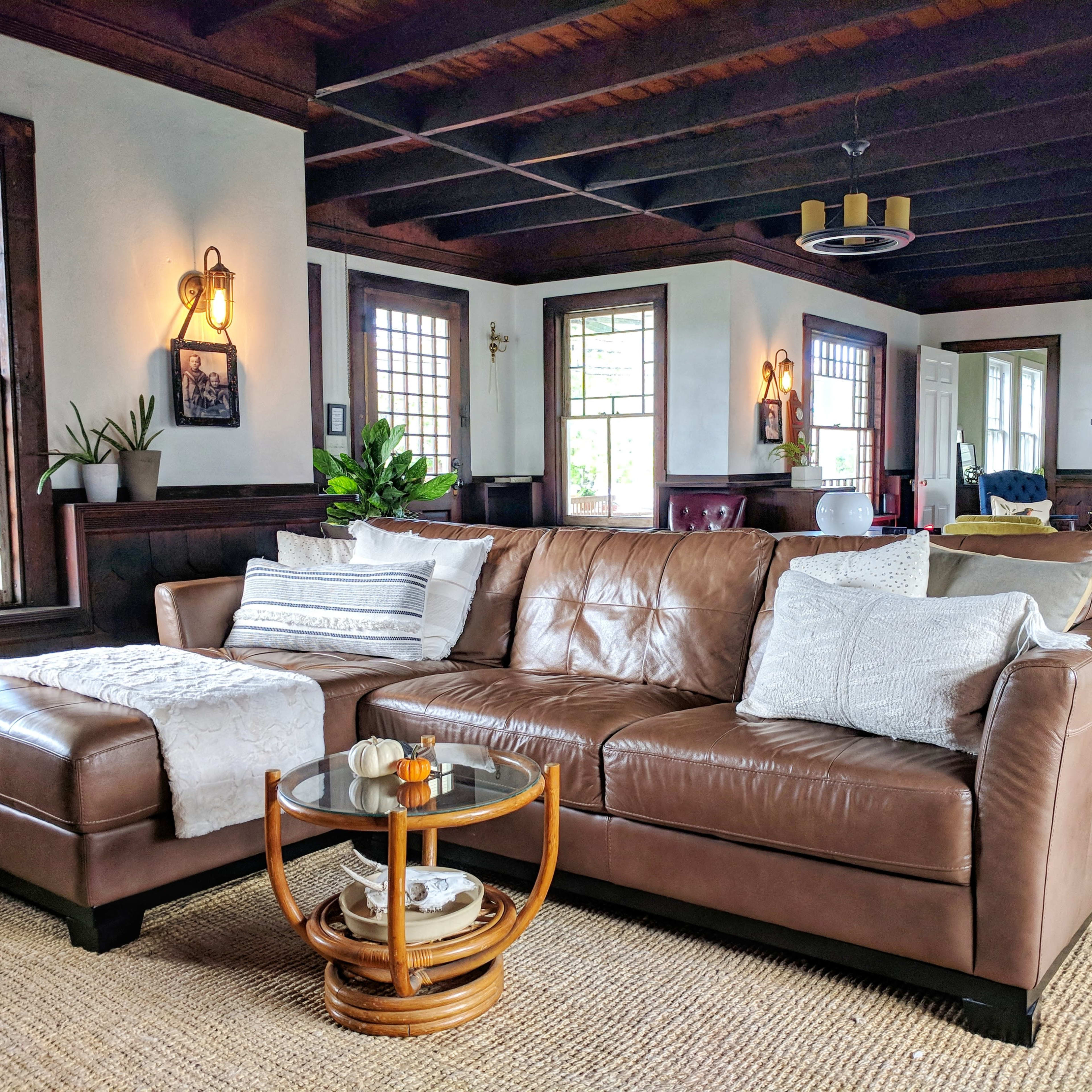 A brown leather sectional couch is positioned in a living room featuring wooden beams, large windows, and a fireplace.