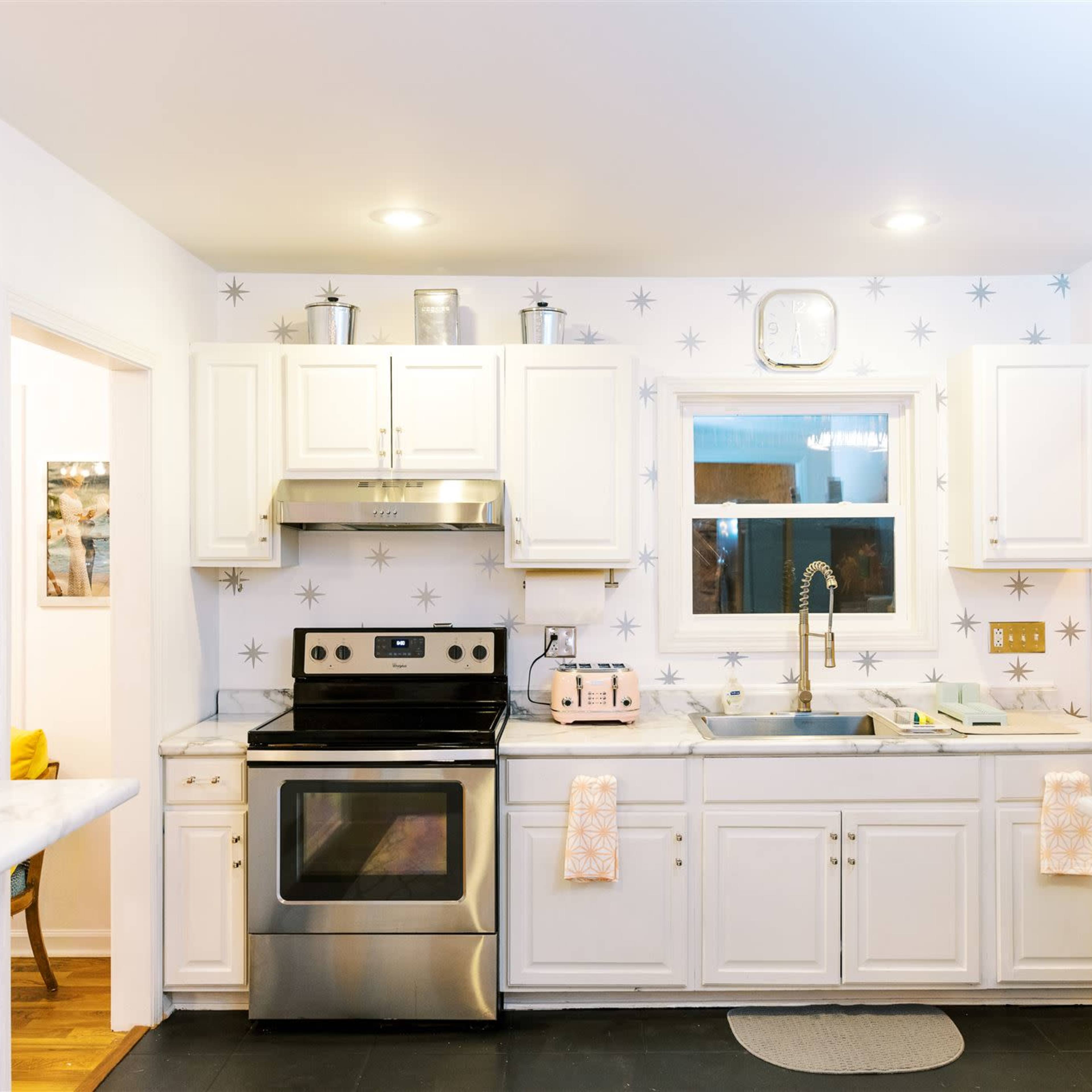 A modern kitchen features white cabinetry, stainless steel appliances, and a marble countertop with a window above the sink.