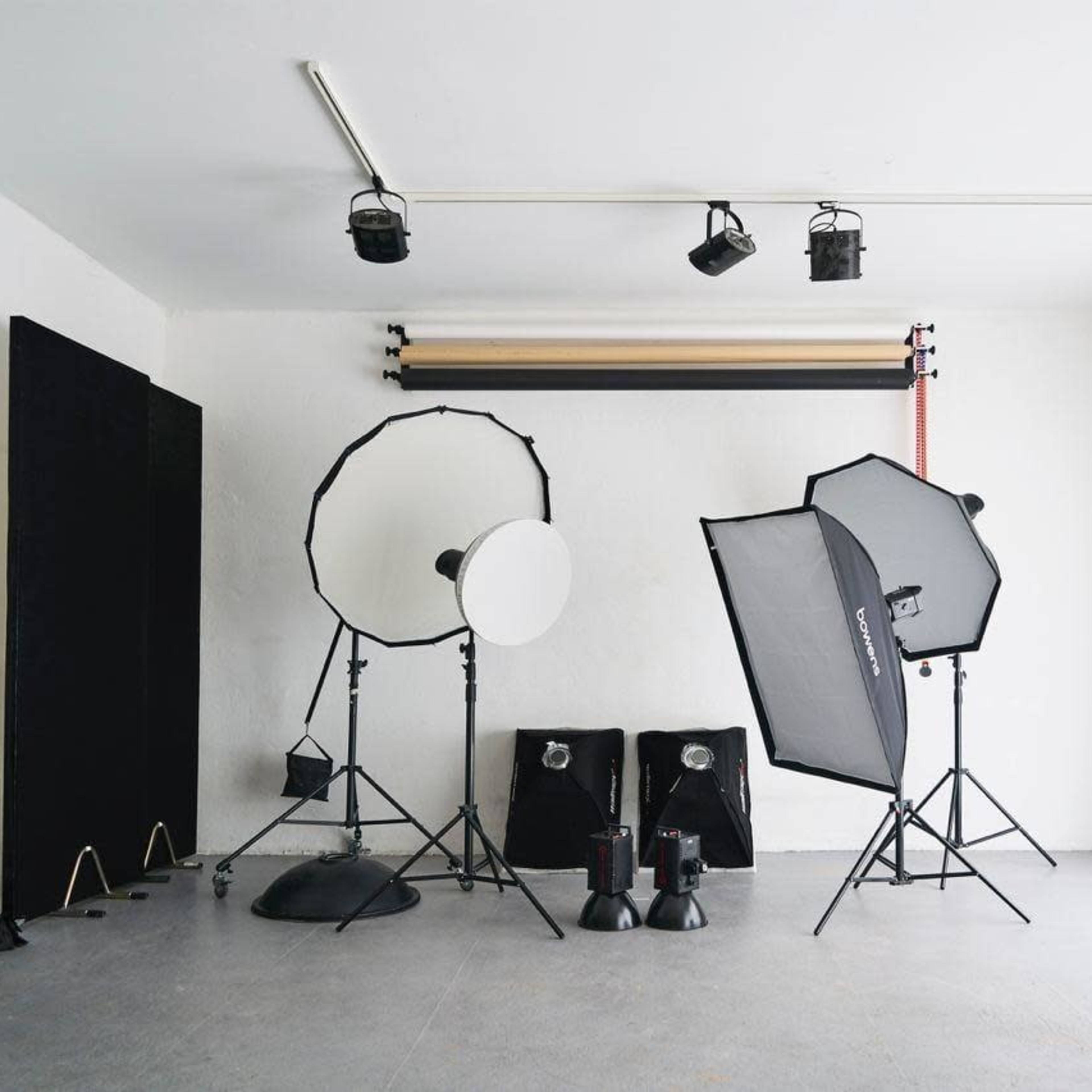 A photography studio is set up with various lighting equipment, including softboxes, reflectors, and background rolls.