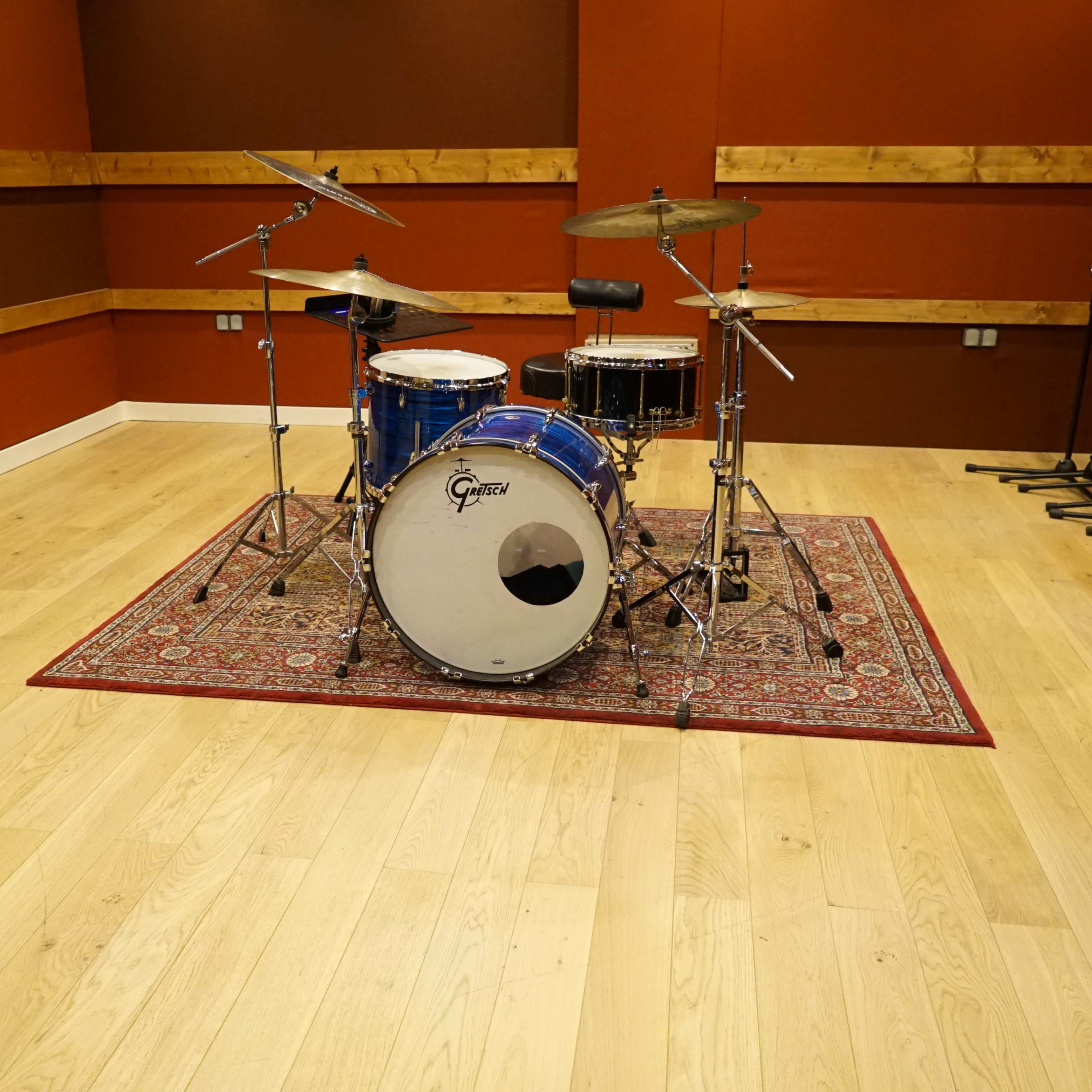A drum set is positioned on a patterned rug within a soundproof room featuring wooden wall panels and polished wooden flooring.