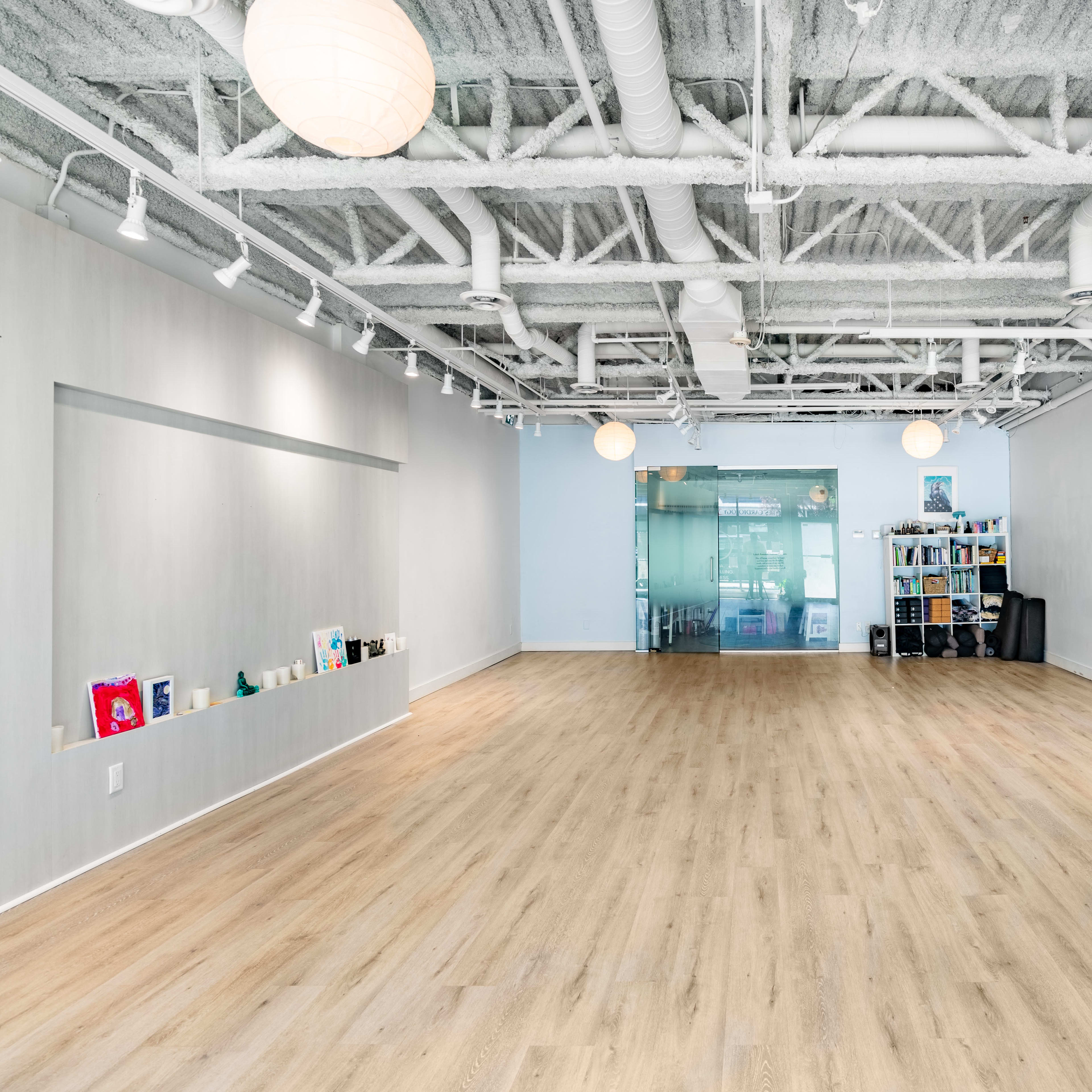 A spacious, well-lit interior room with light wooden flooring and shelves filled with books at one end.
