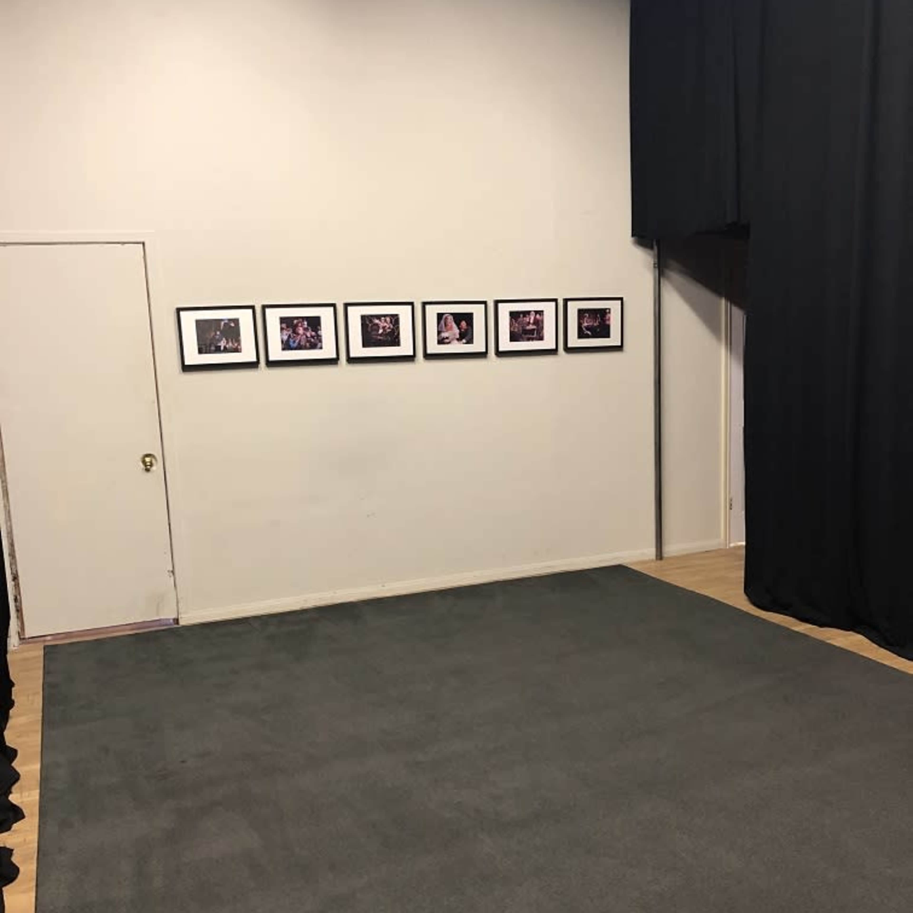 A clean room with a gray carpet features a wall adorned with eight framed photographs and a closed door on the side.
