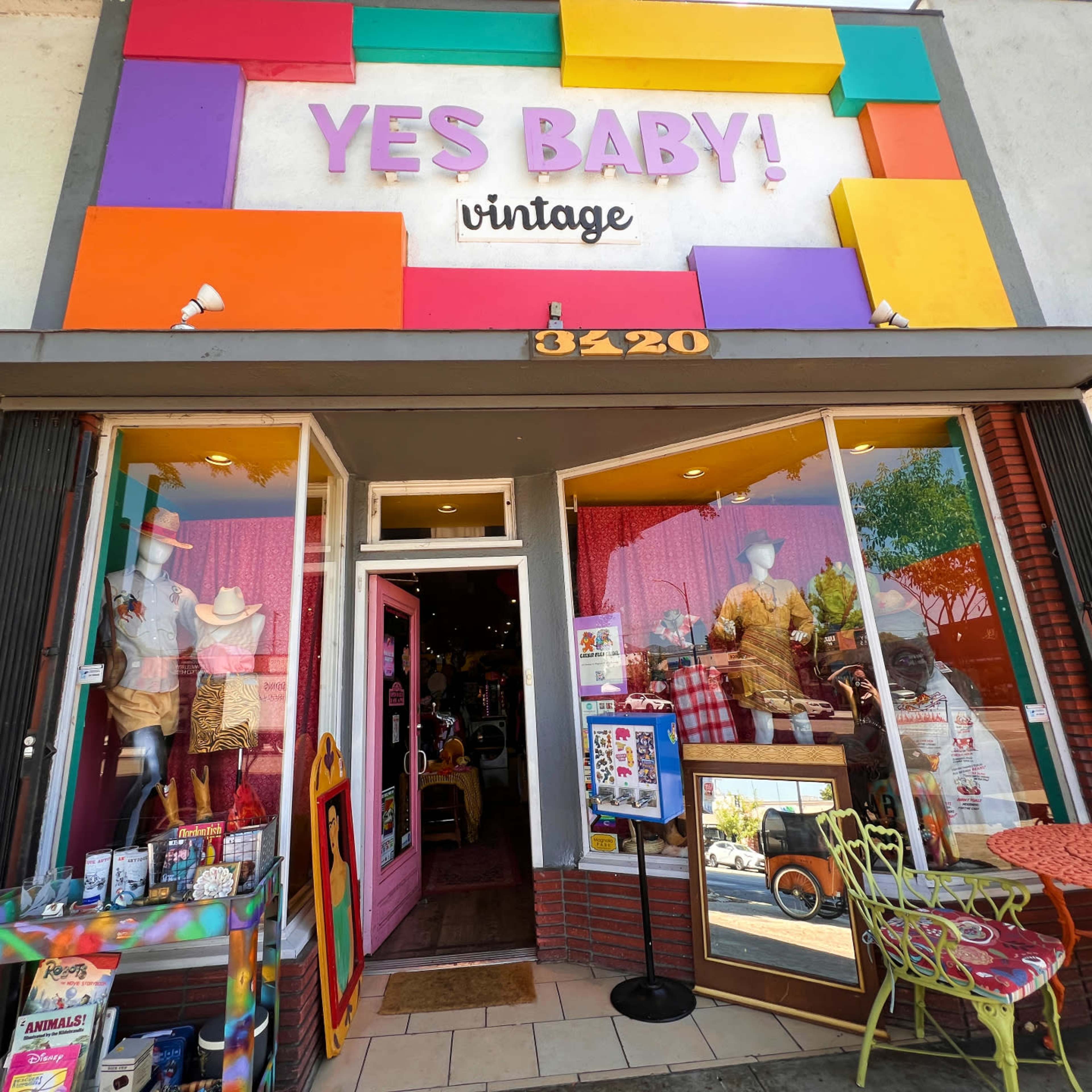 A vintage storefront with colorful signage and a display window featuring mannequins dressed in retro clothing.