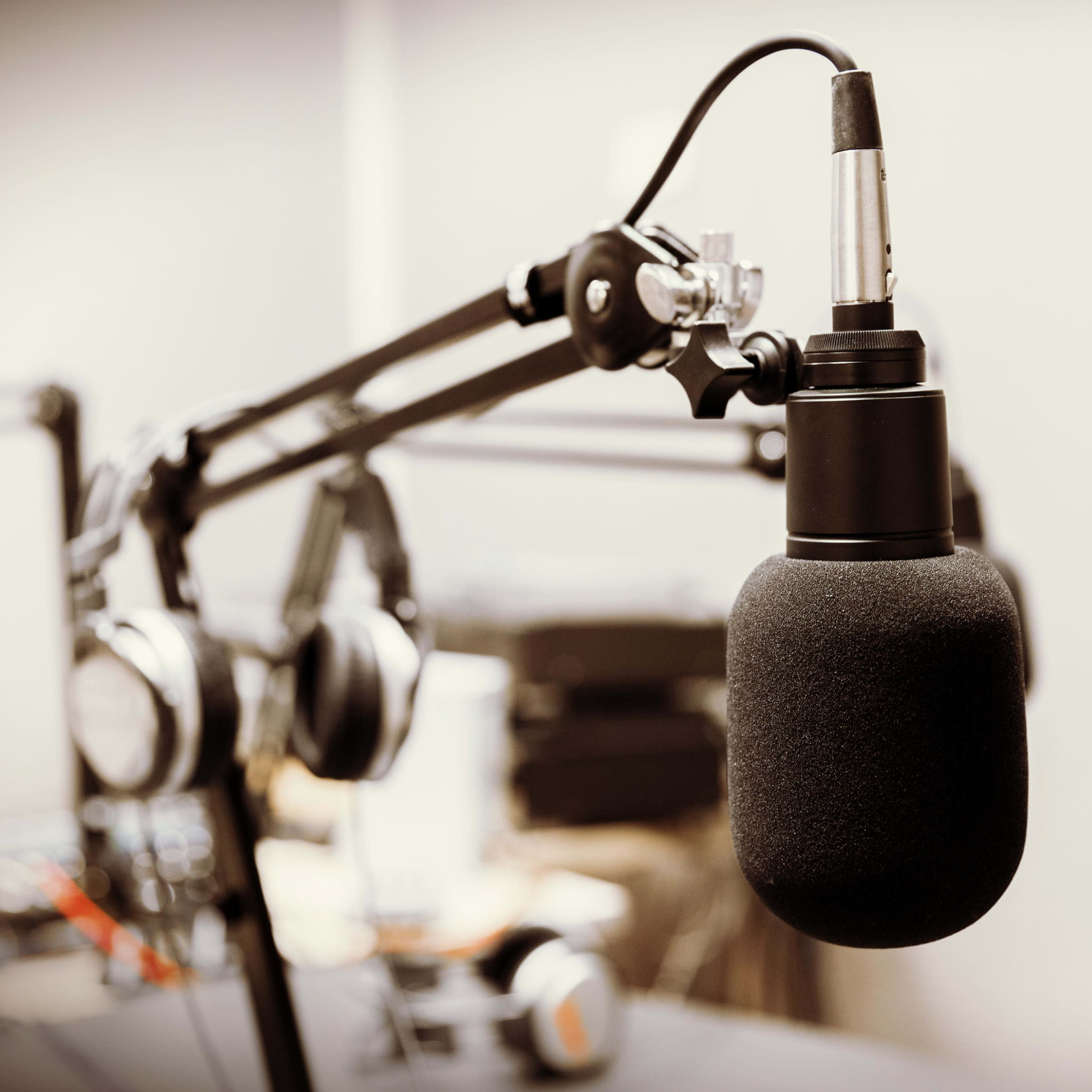 A microphone is mounted on a flexible arm in a recording studio, with headphones visible in the background.