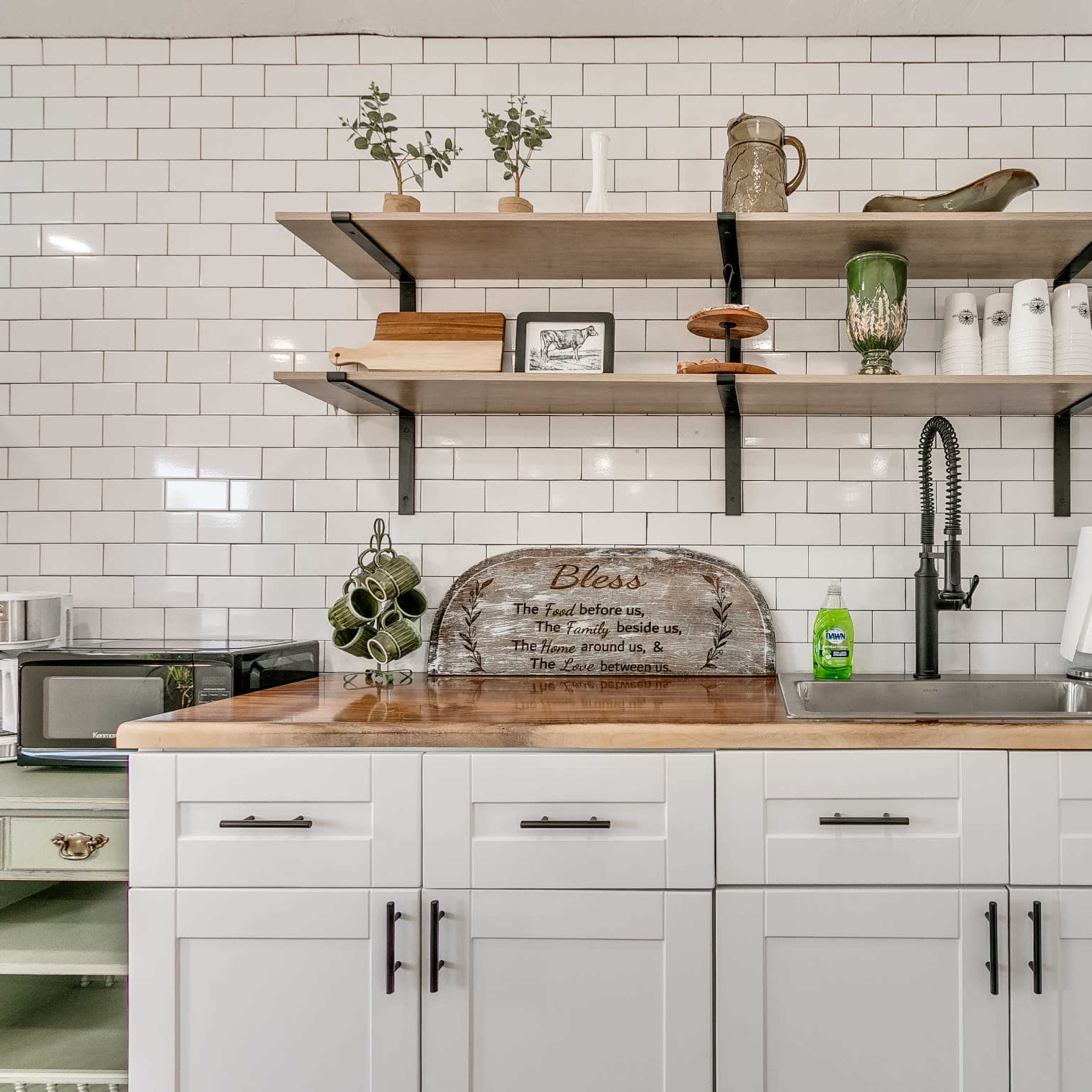 A modern kitchen with white cabinetry, open shelves displaying decorative items, and a countertop with a sink and kitchen appliances.