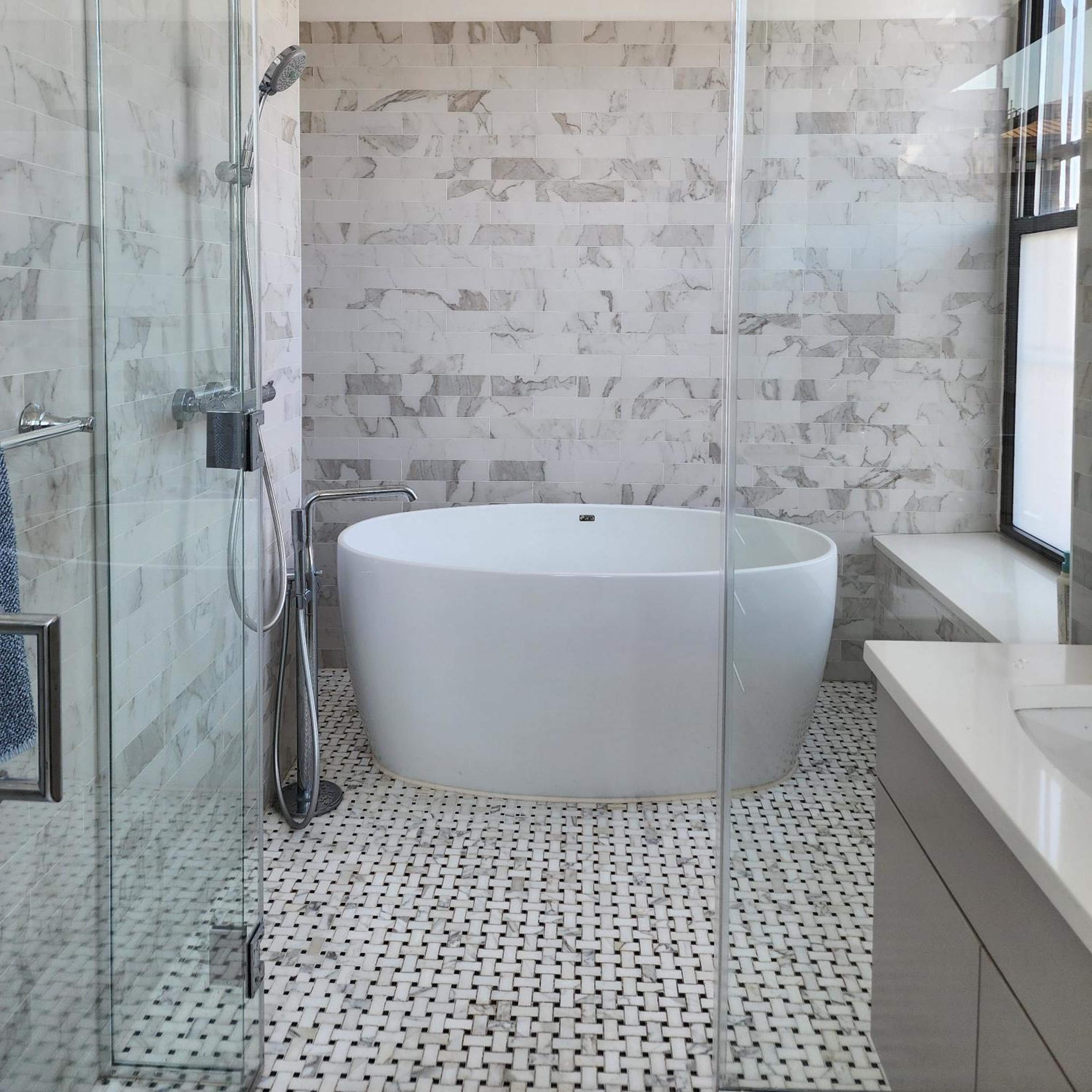 A modern bathroom featuring a glass shower, a freestanding white bathtub, and tiled walls and flooring.