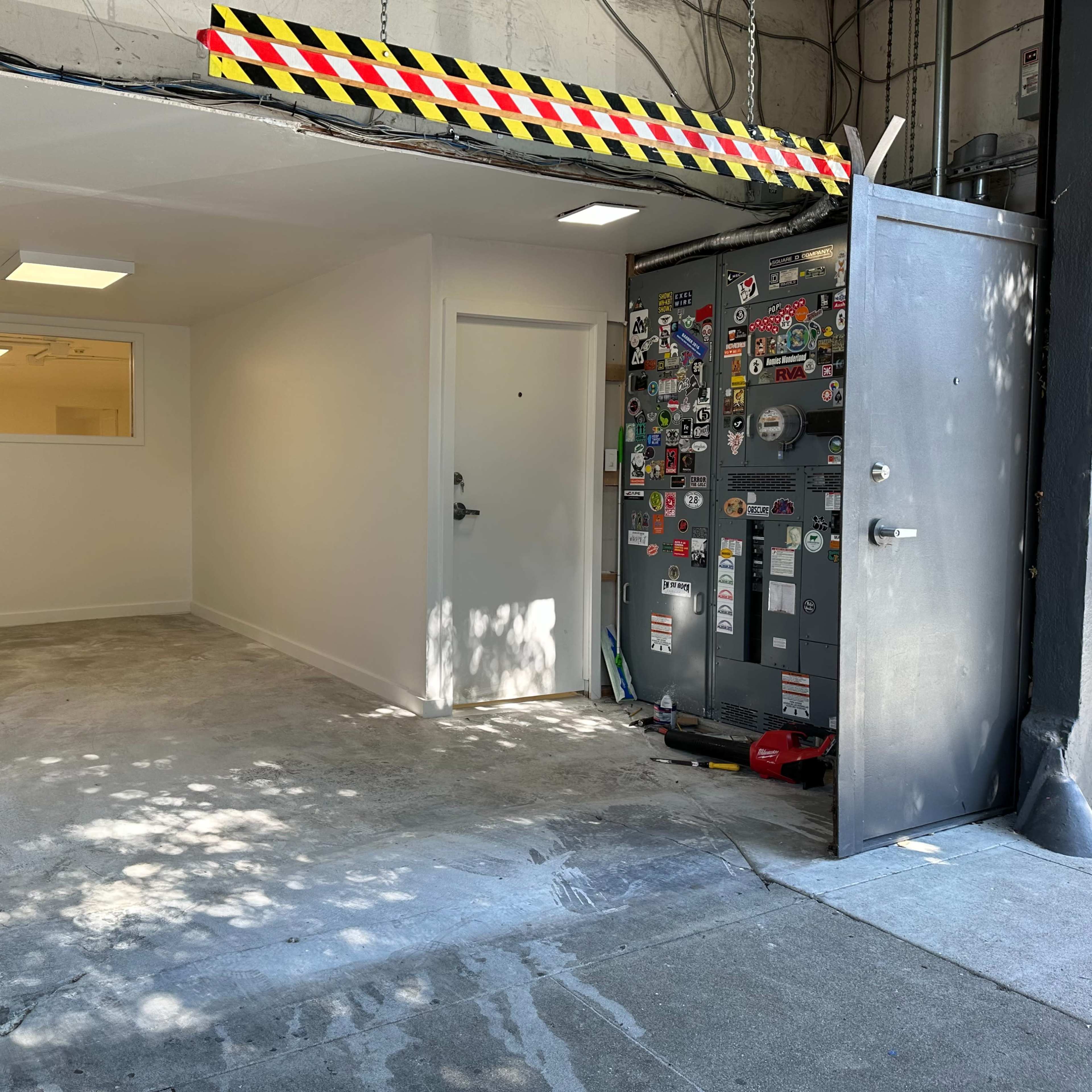 An empty garage with a white wall and a door, featuring a utility panel covered in various stickers next to it.