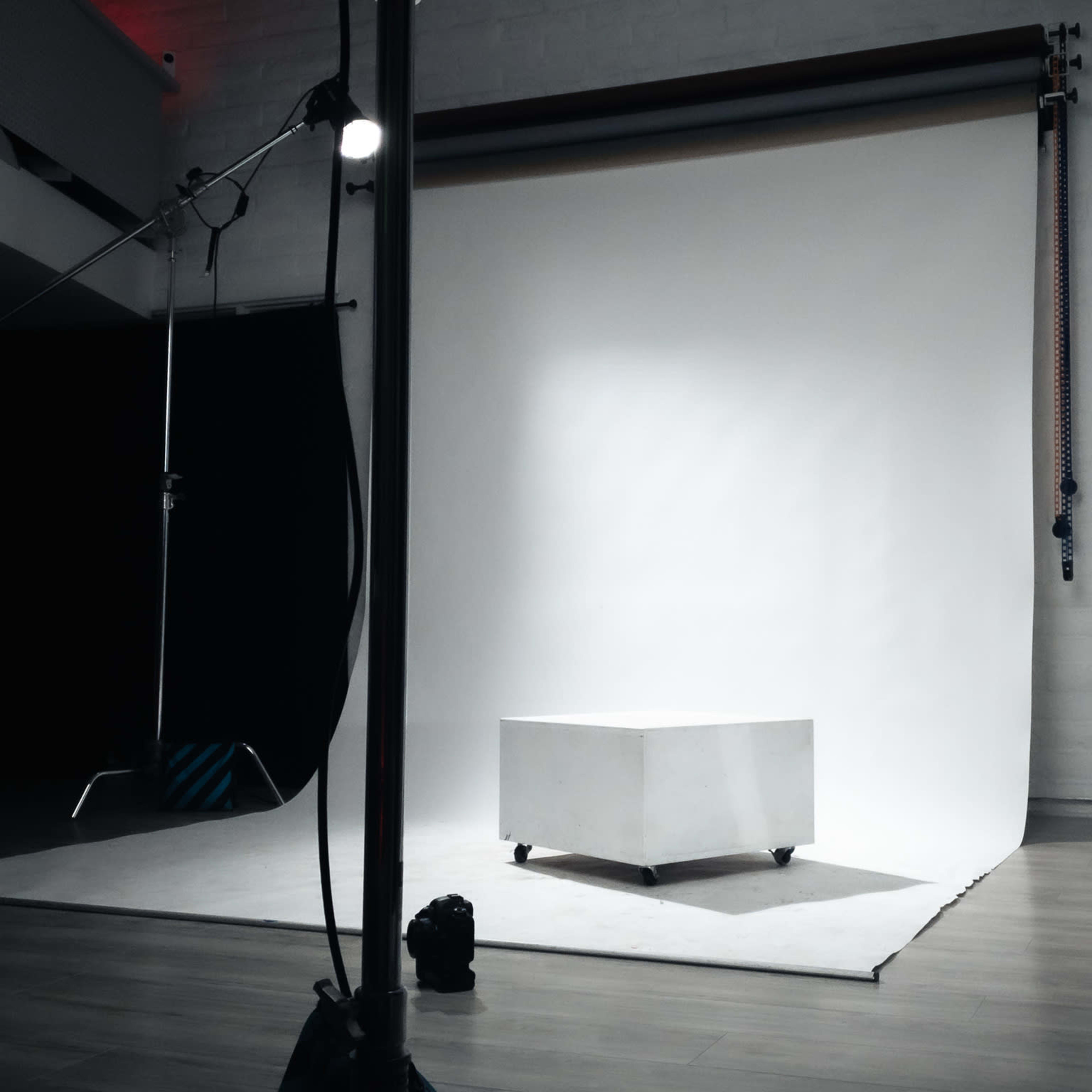 A white studio backdrop is set up with a small white box on wheels in the center of the room, surrounded by lighting equipment.