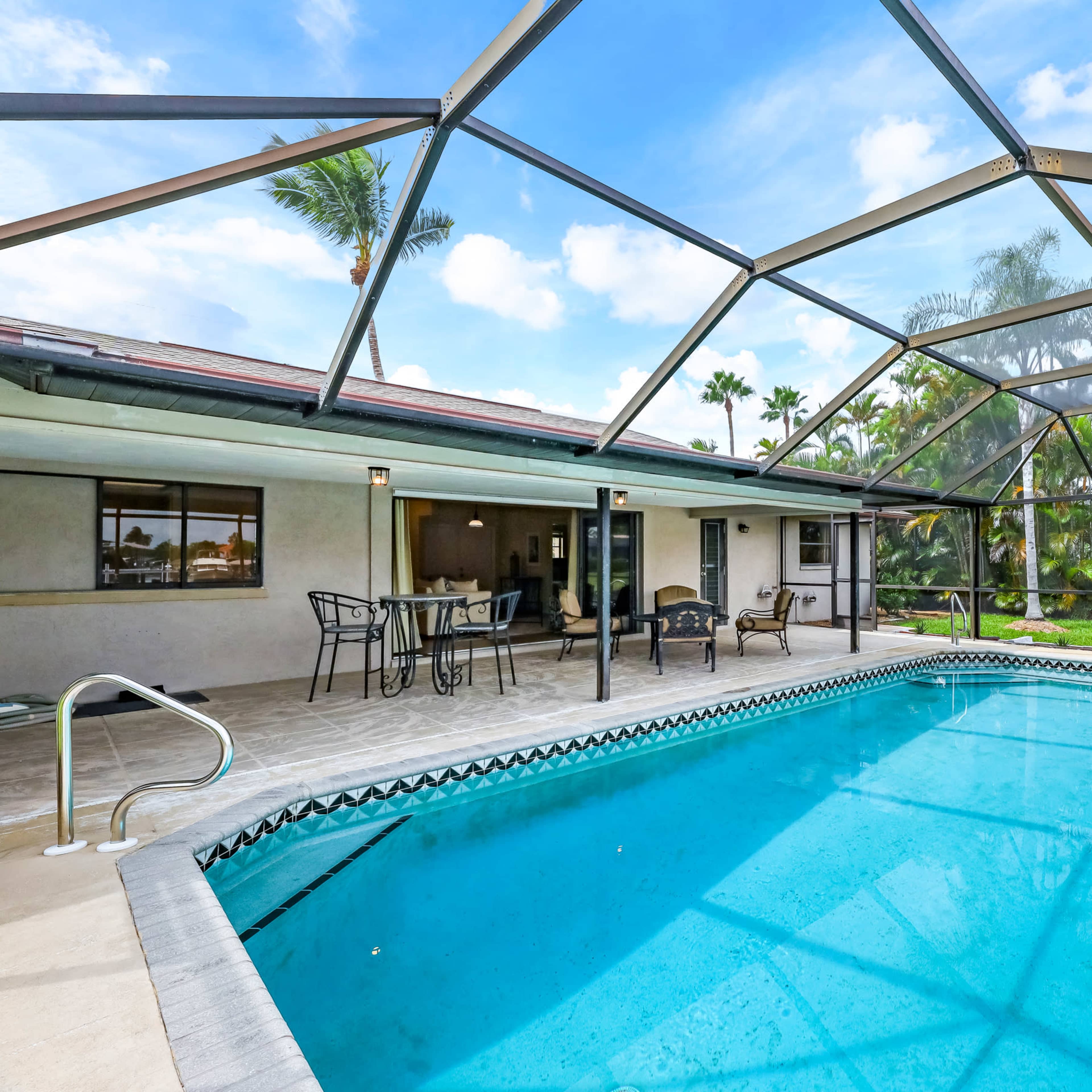A backyard with a screened-in pool area, featuring a rectangular swimming pool and patio furniture nearby.