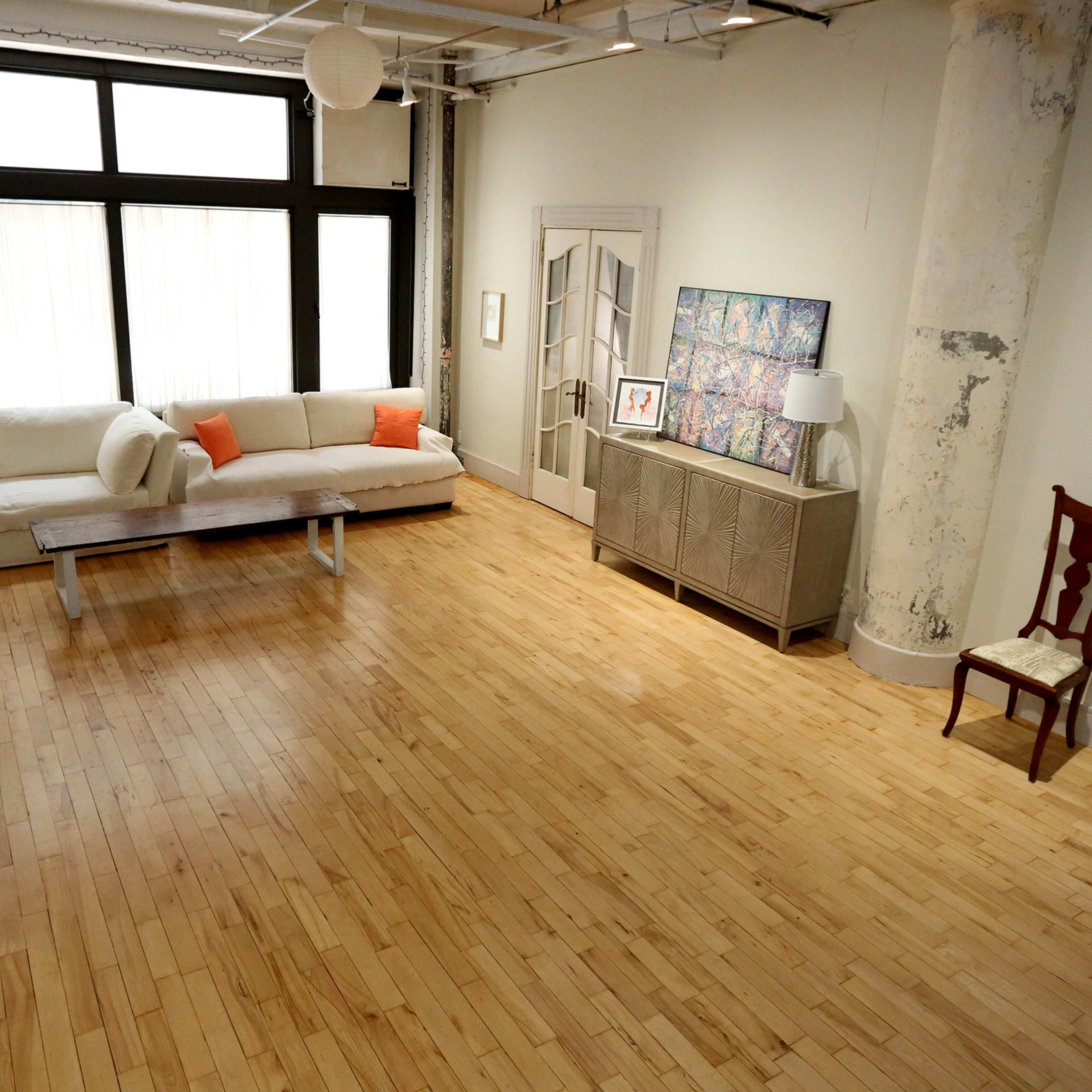 A spacious, modern living room with a light-colored sofa, a wooden coffee table, a cabinet, and a single chair against a wall.