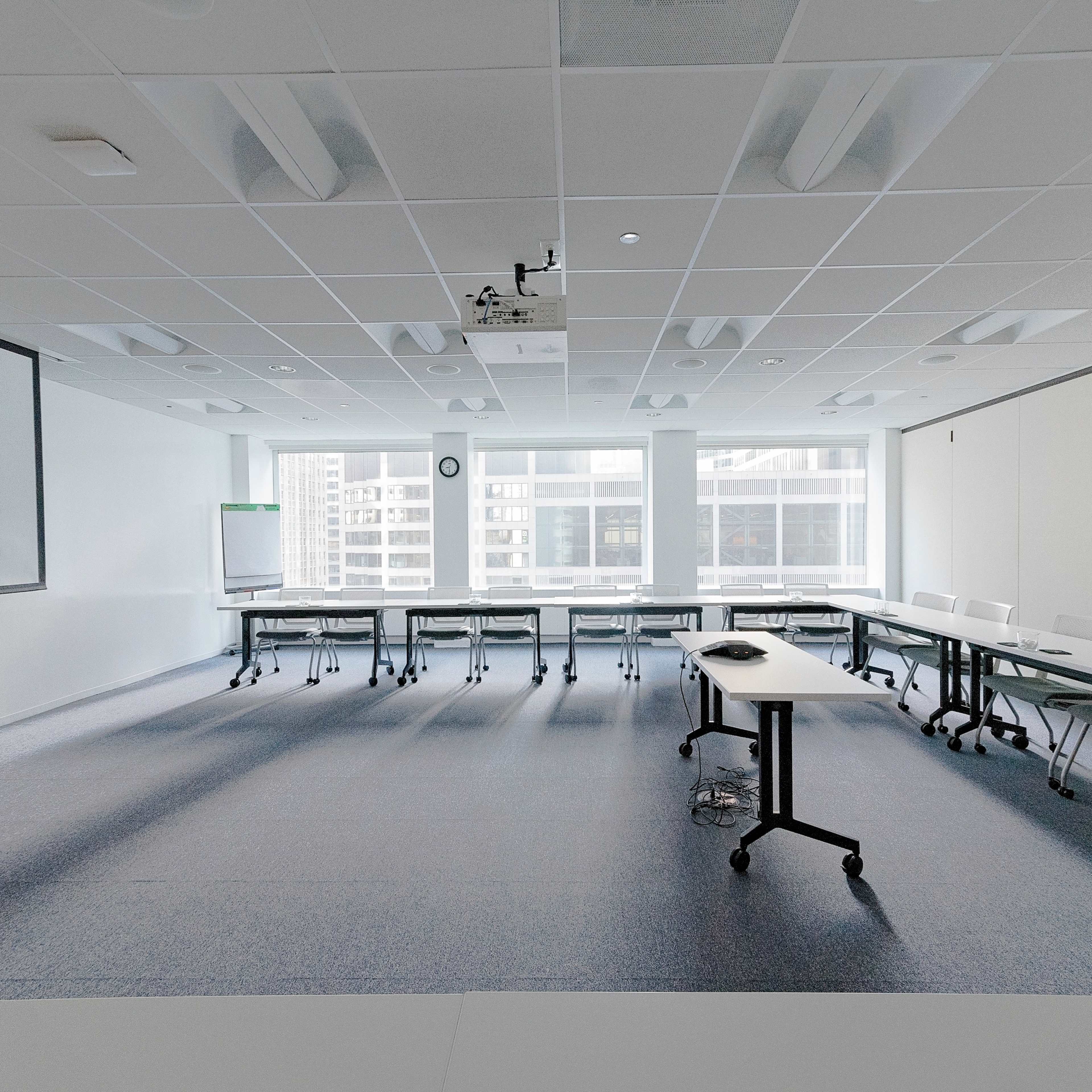 A modern conference room features rows of tables and chairs with large windows providing a view of the city skyline.