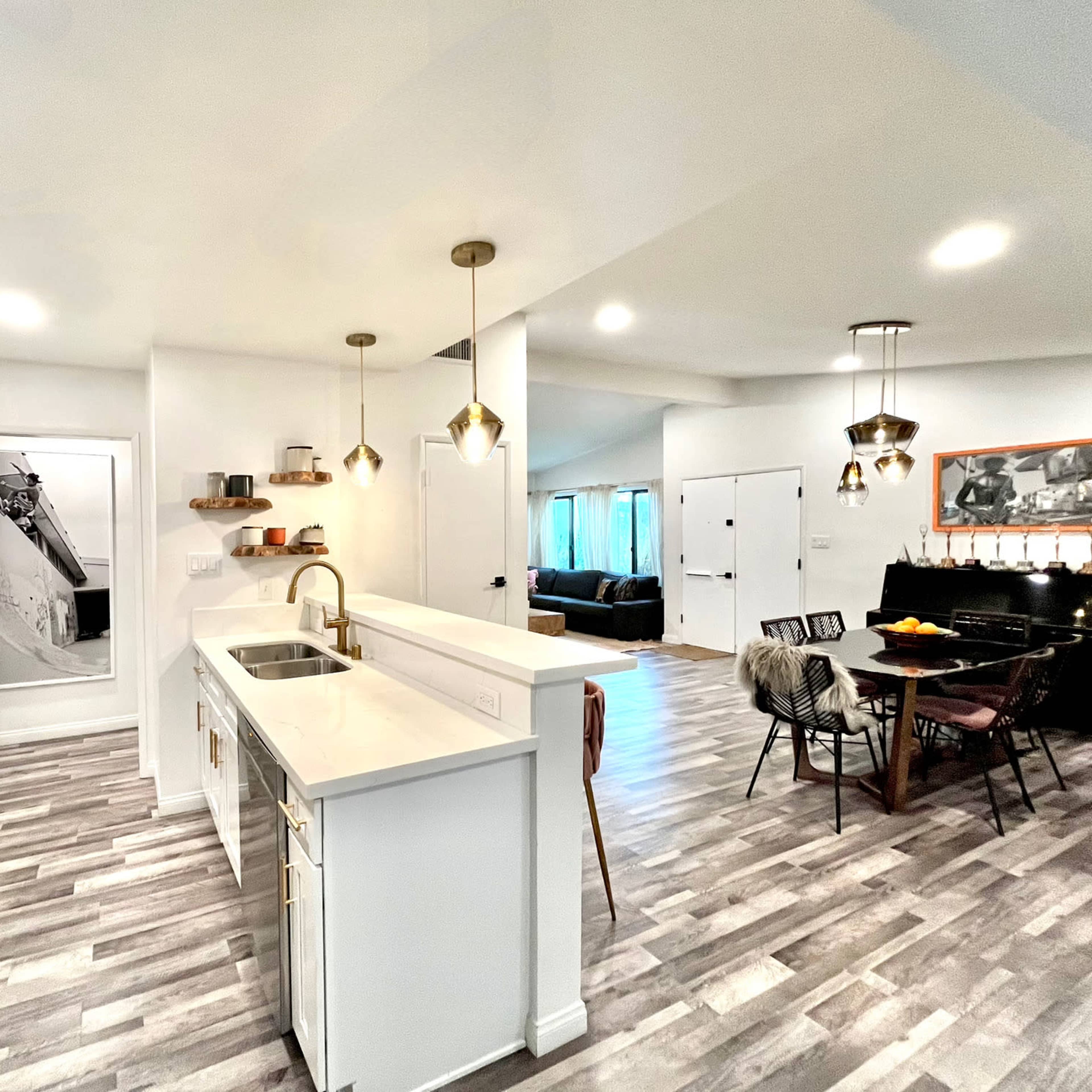 A modern kitchen with white cabinetry, pendant lights, and a dining area in an open-concept layout.