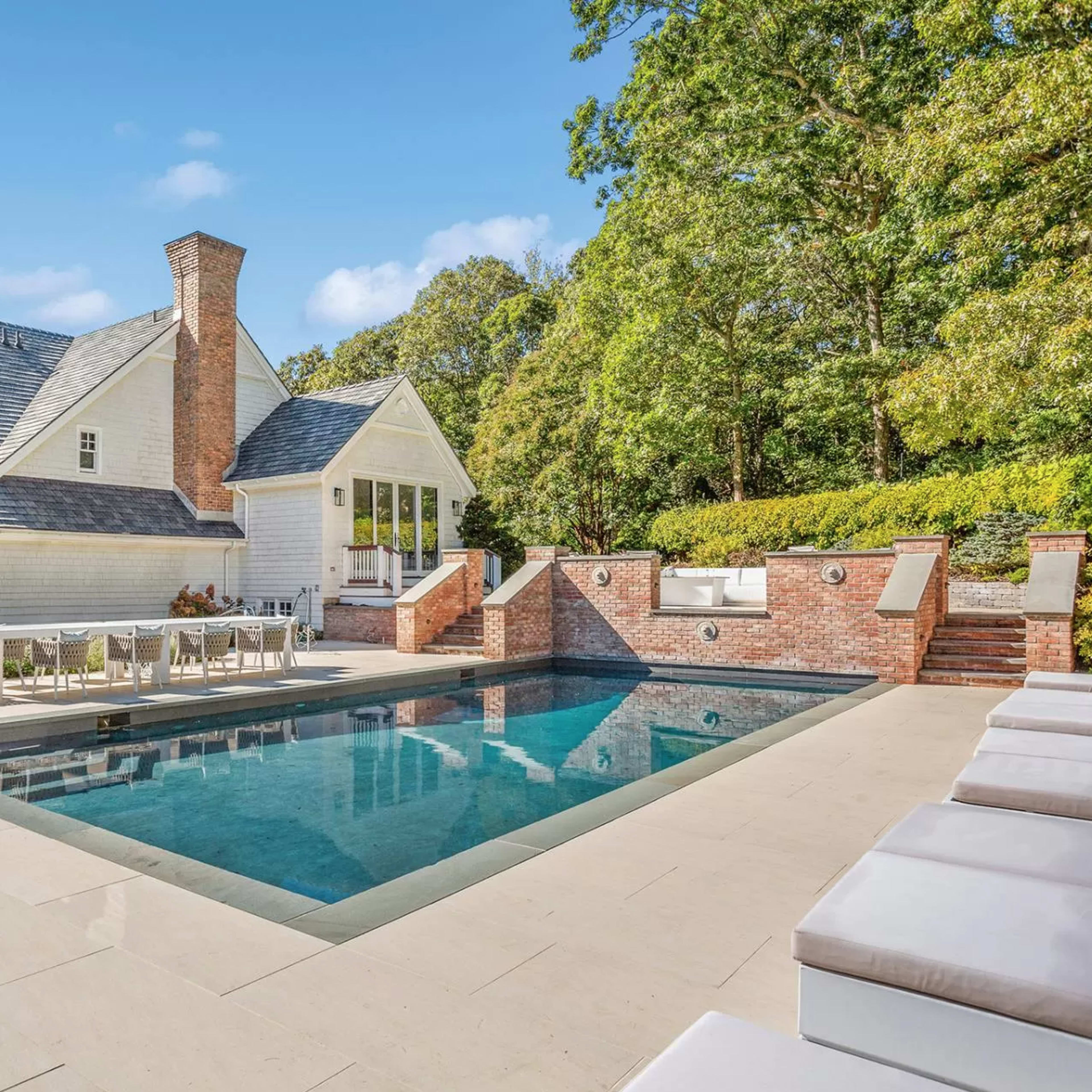 A modern home with a large swimming pool and a patio area surrounded by trees and landscaping.