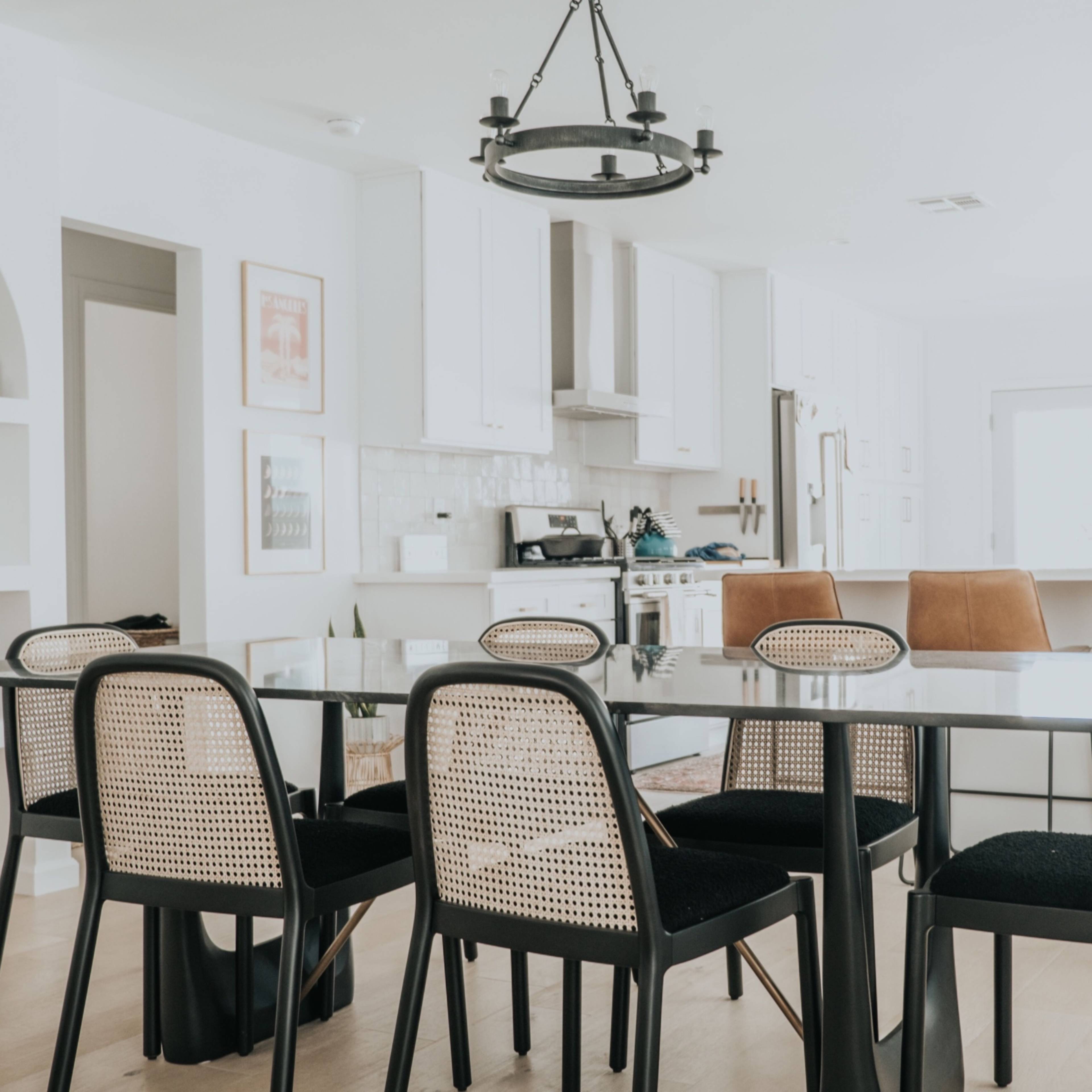 A modern dining area features a glass table surrounded by black and tan chairs, with a kitchen visible in the background.