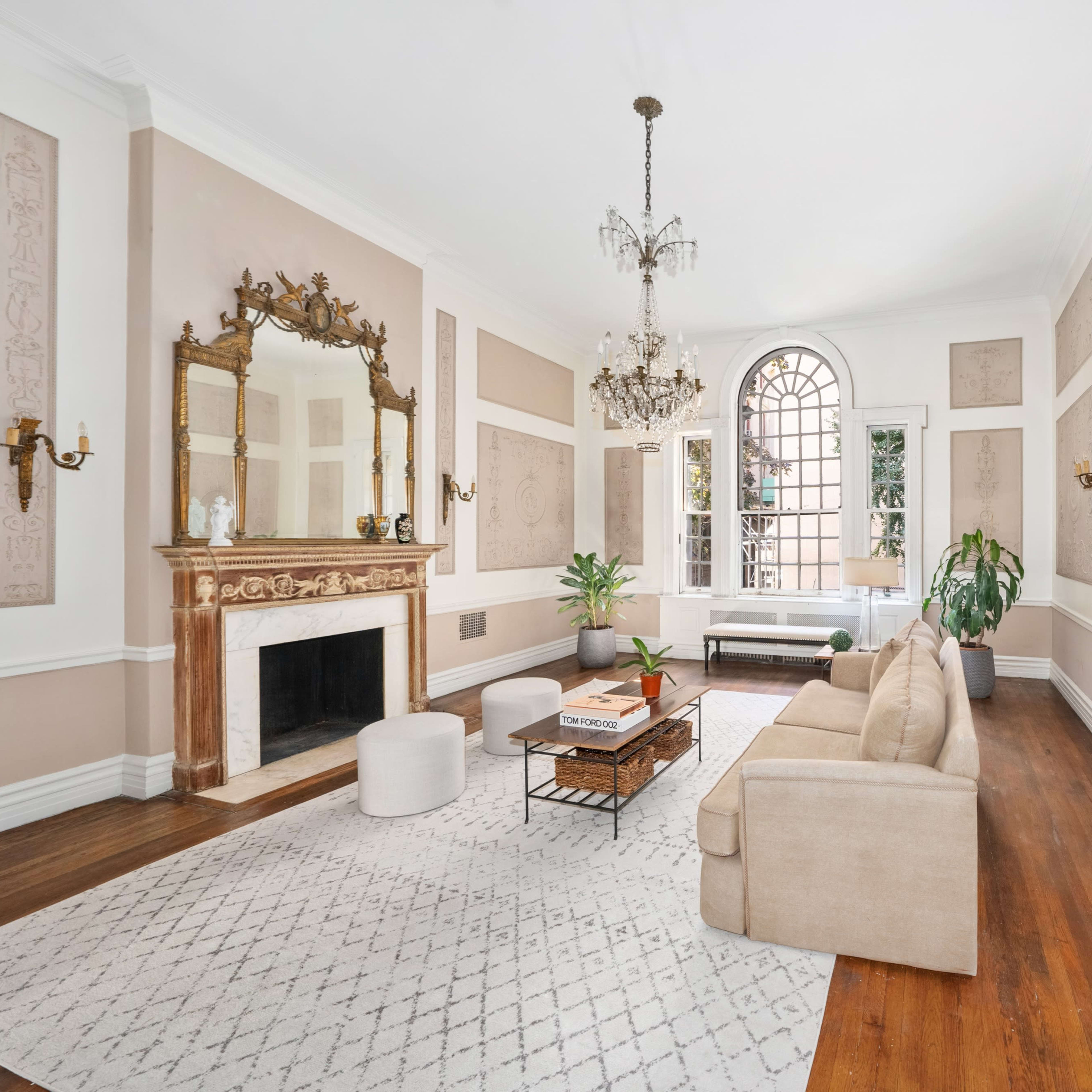 A spacious living room with a beige sofa, a coffee table on a light-colored rug, a fireplace, and large windows allowing natural light to enter.