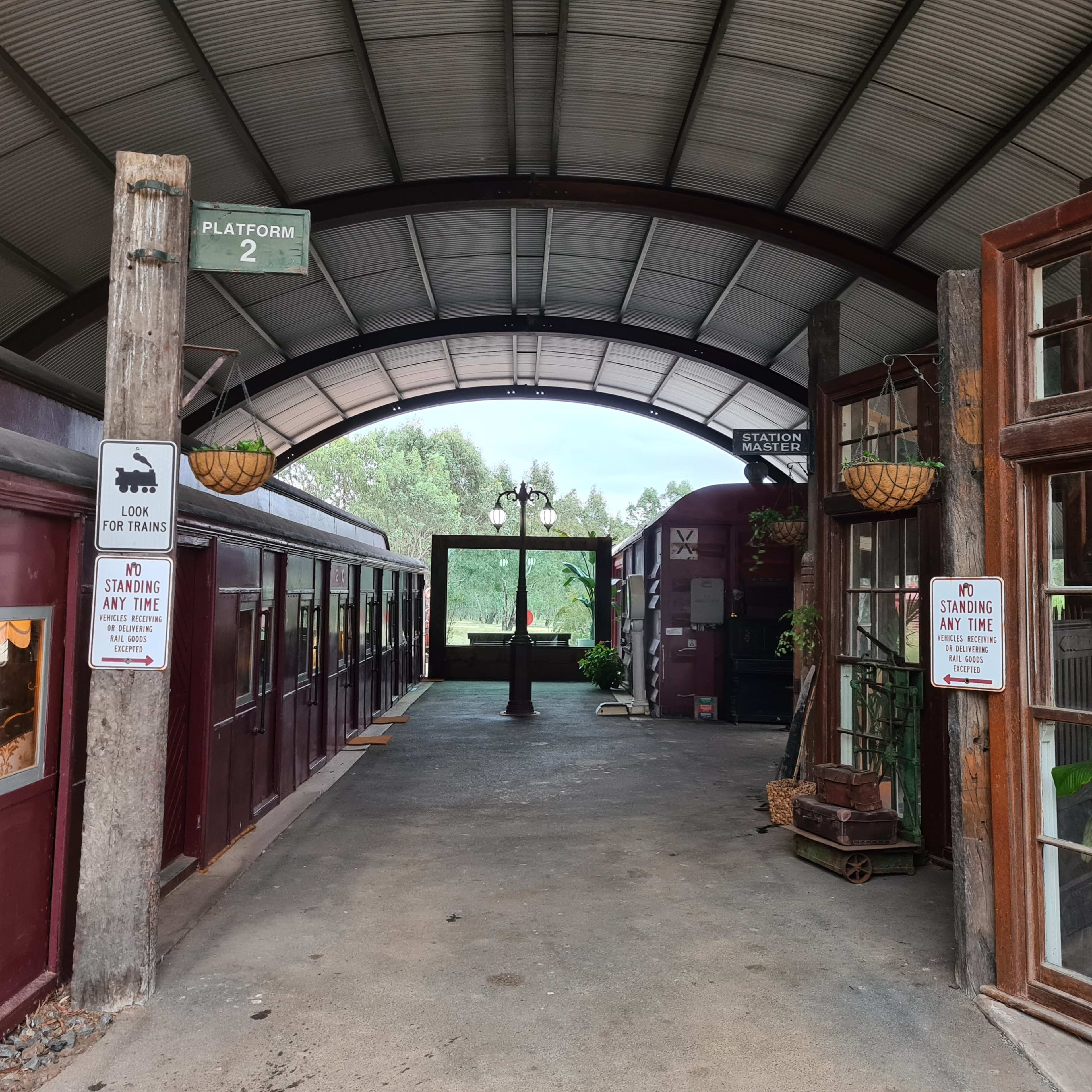 An open-air train station with wooden stalls and signs indicating the platform and standing area.