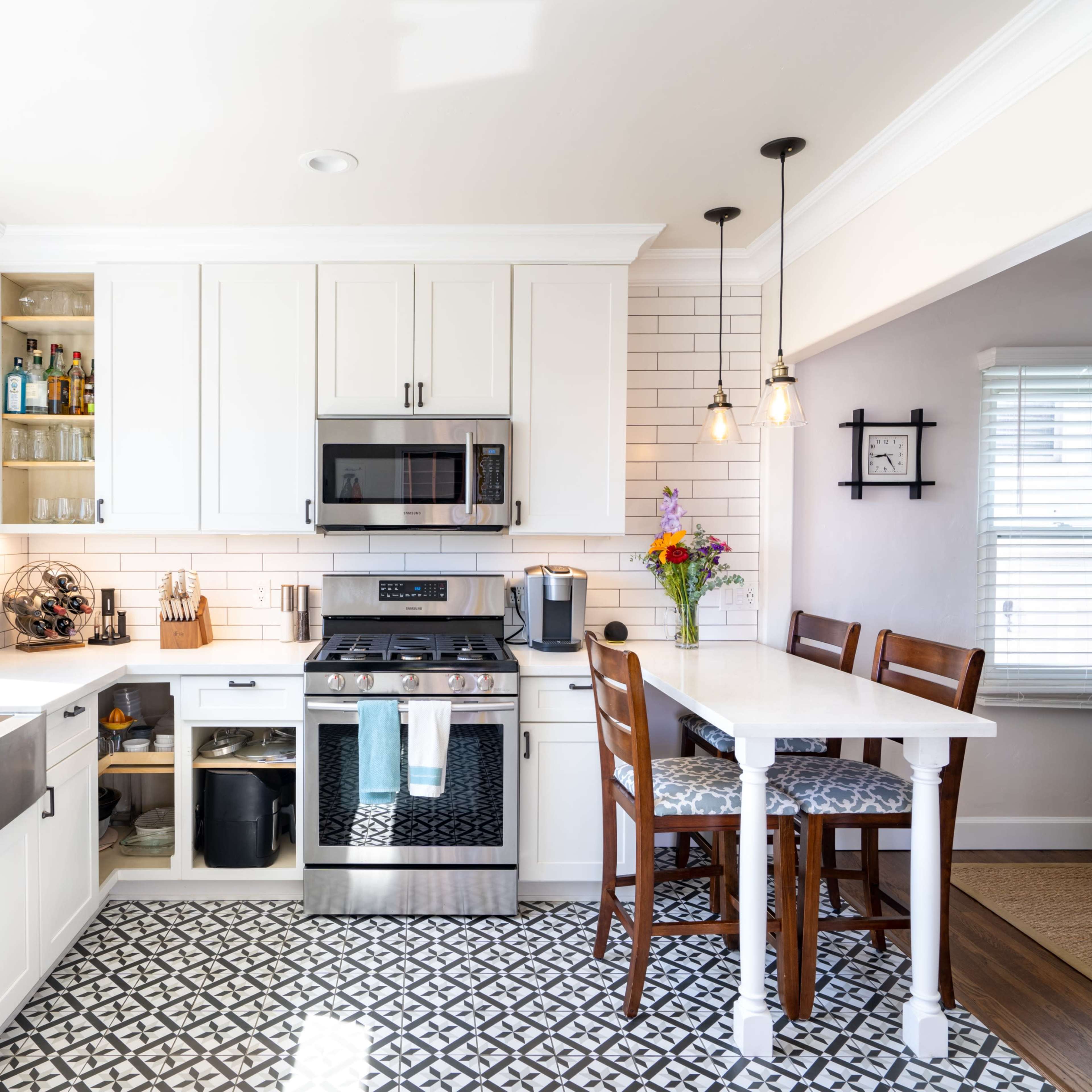A modern kitchen features white cabinetry, stainless steel appliances, and a patterned floor, with a small dining area set for four.