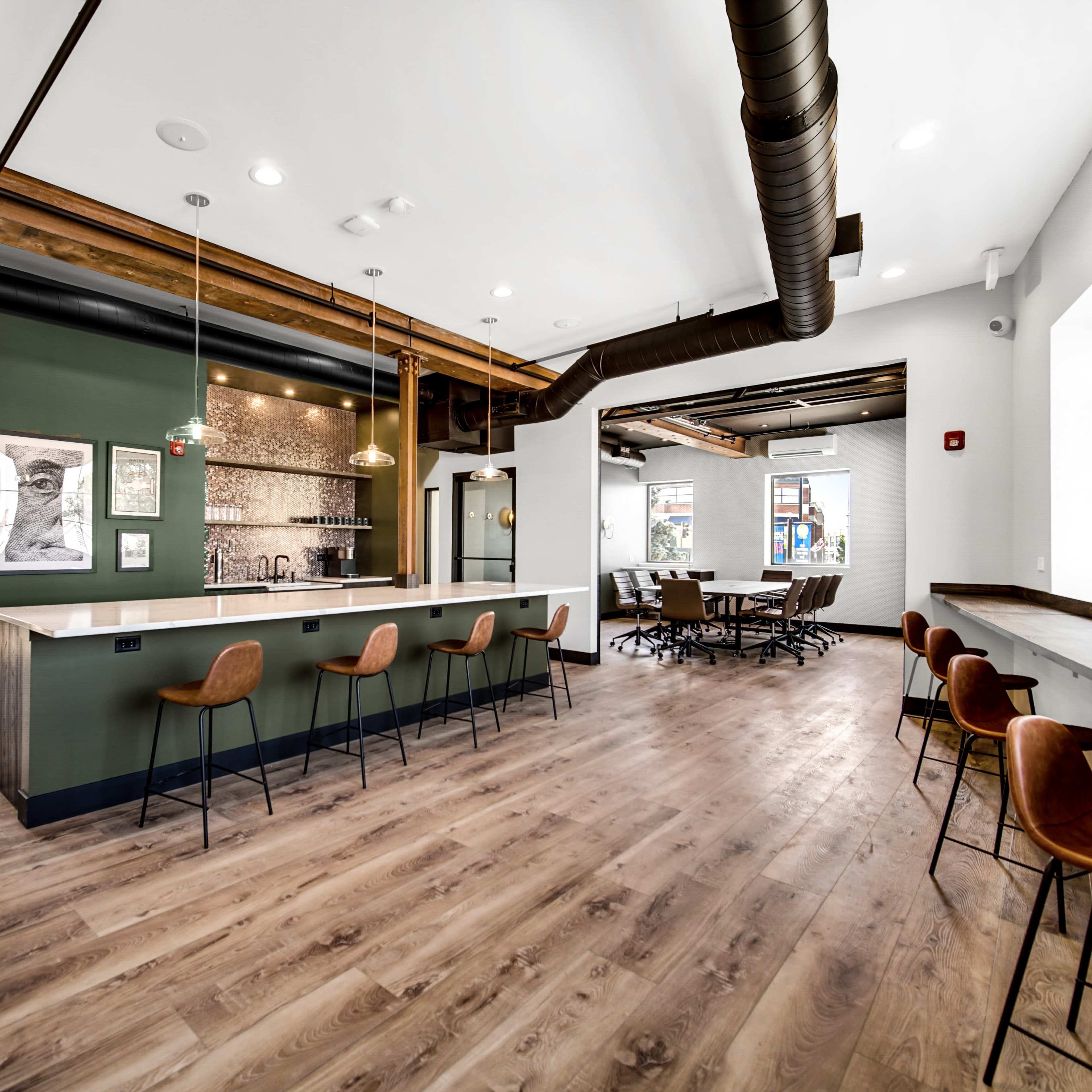 A modern office space with a bar area and a conference room featuring wooden flooring and industrial design elements.