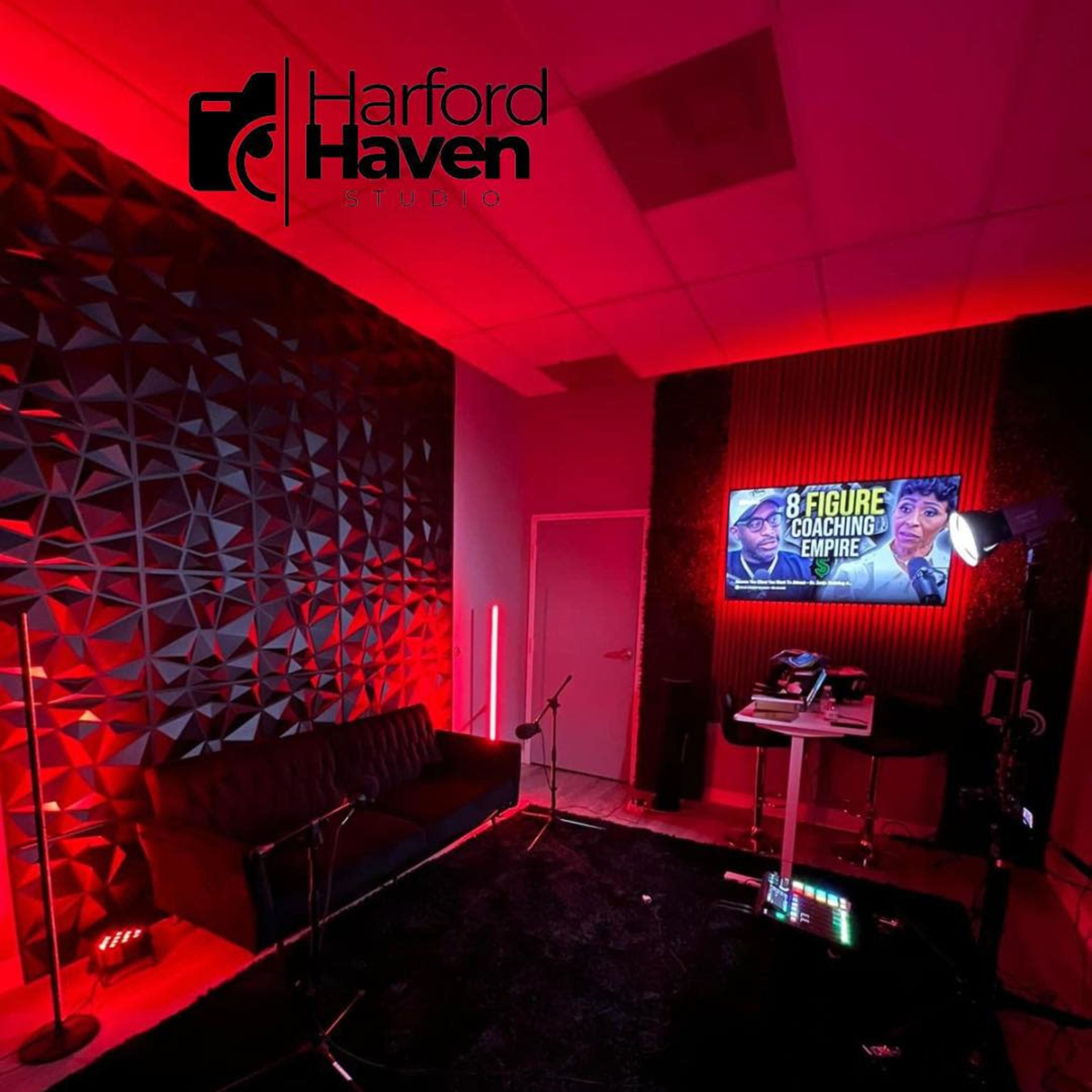 A modern studio space features a dark carpet, a sofa, and a television displaying a coaching program, all illuminated by red lighting.