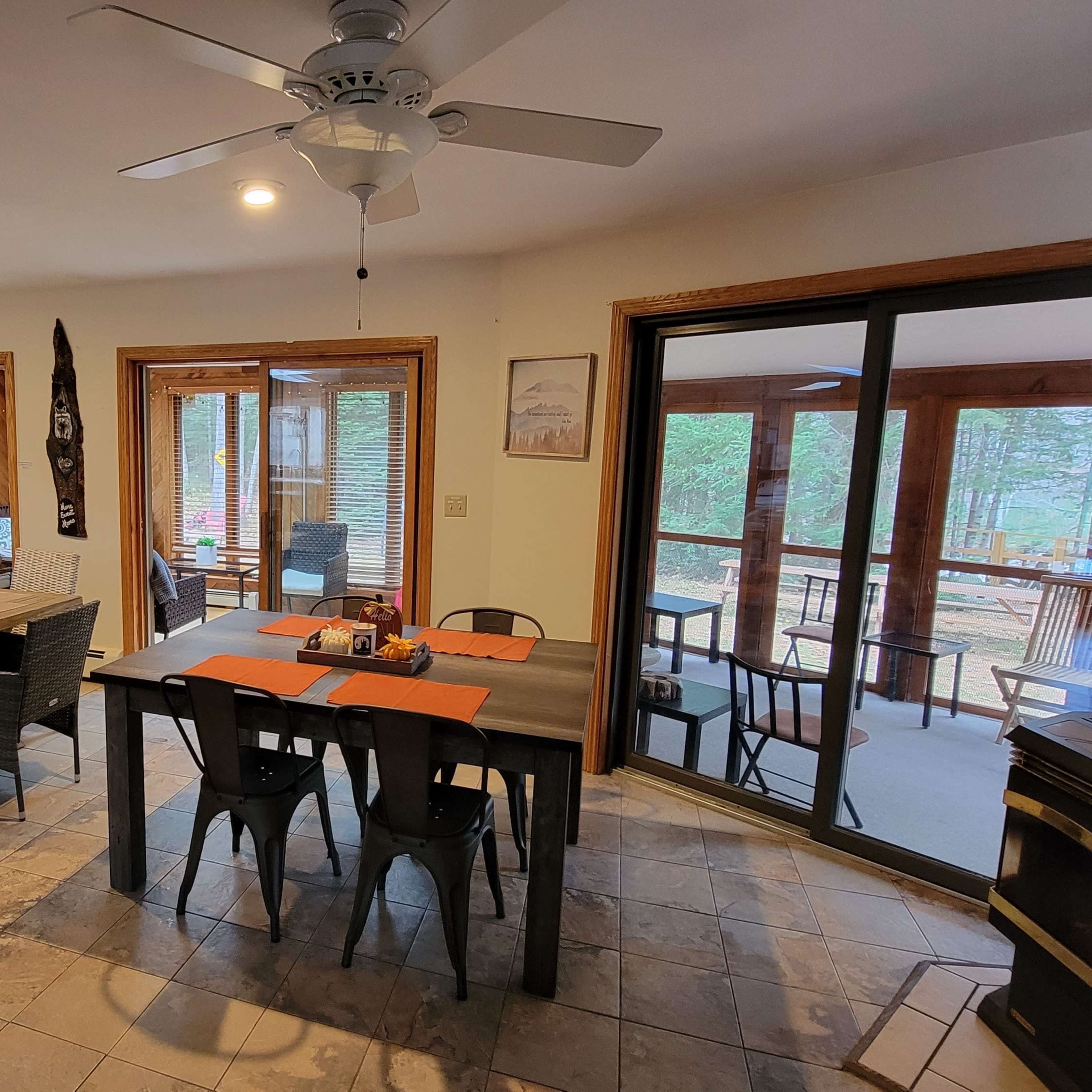 A spacious dining area with a large table set for a meal, surrounded by windows that provide a view of an outdoor porch.