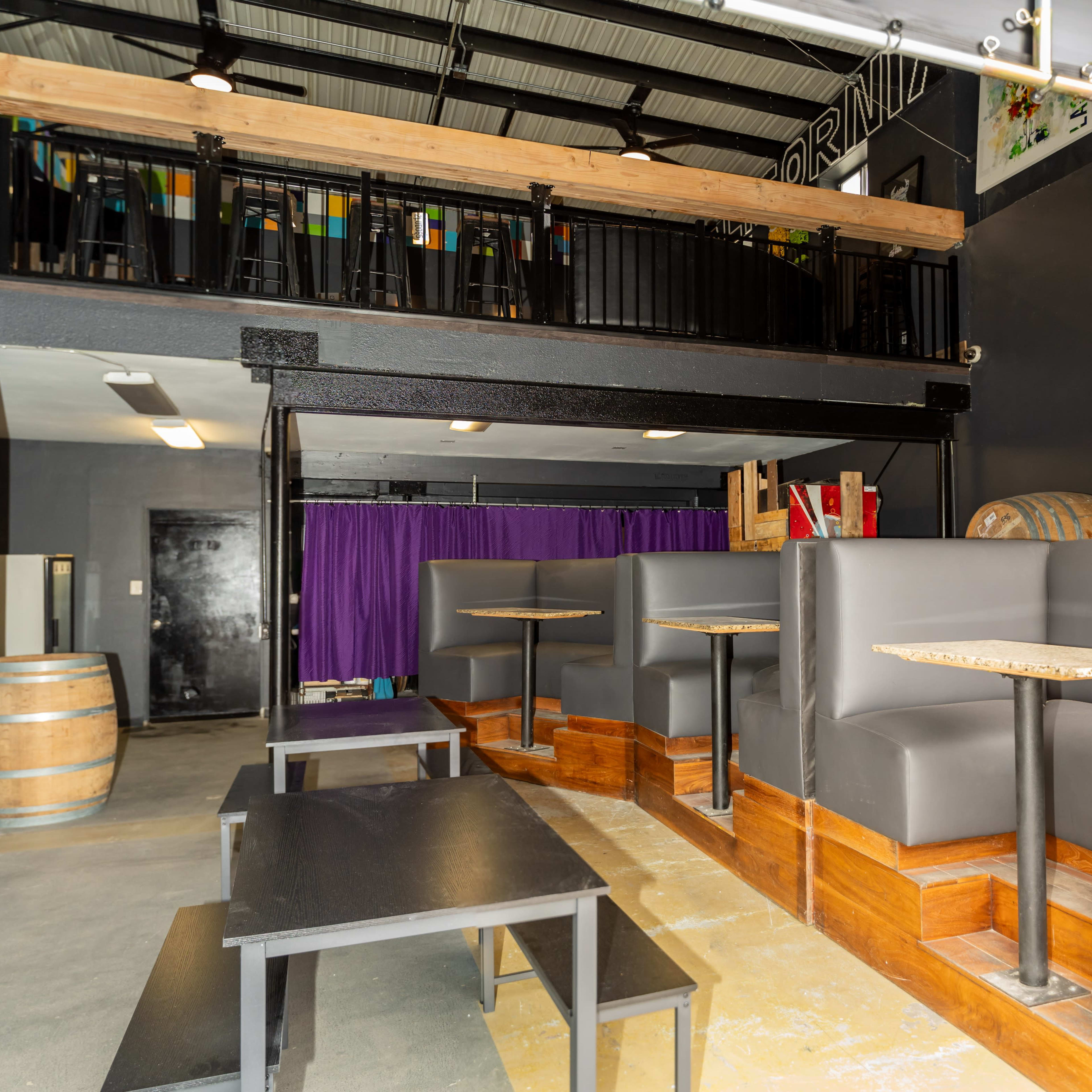 A modern indoor space featuring a two-level seating area with wooden accents, black furniture, and a purple curtain in the background.
