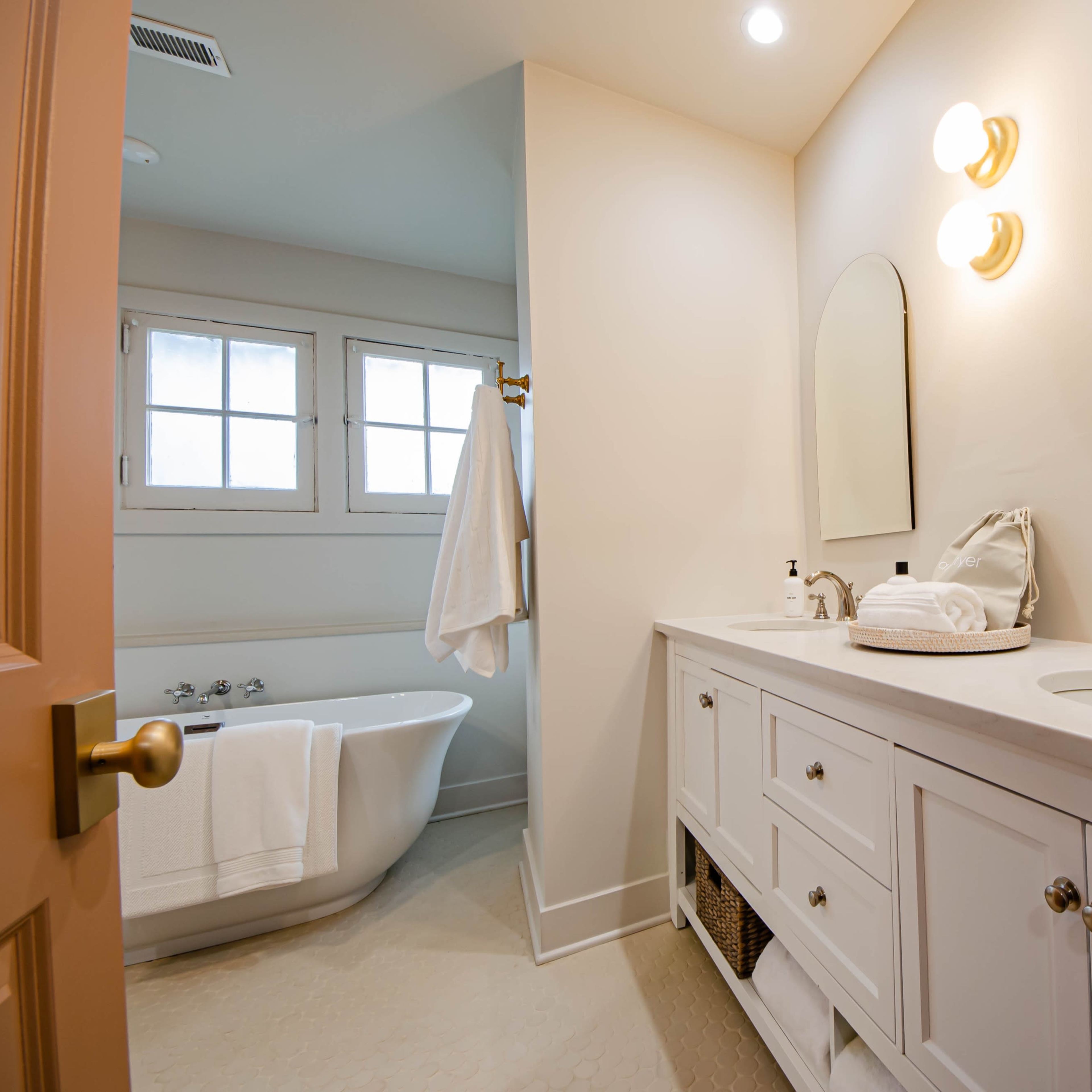 A well-lit bathroom featuring a freestanding tub, a double sink vanity with storage, and two mirrors above the sinks.