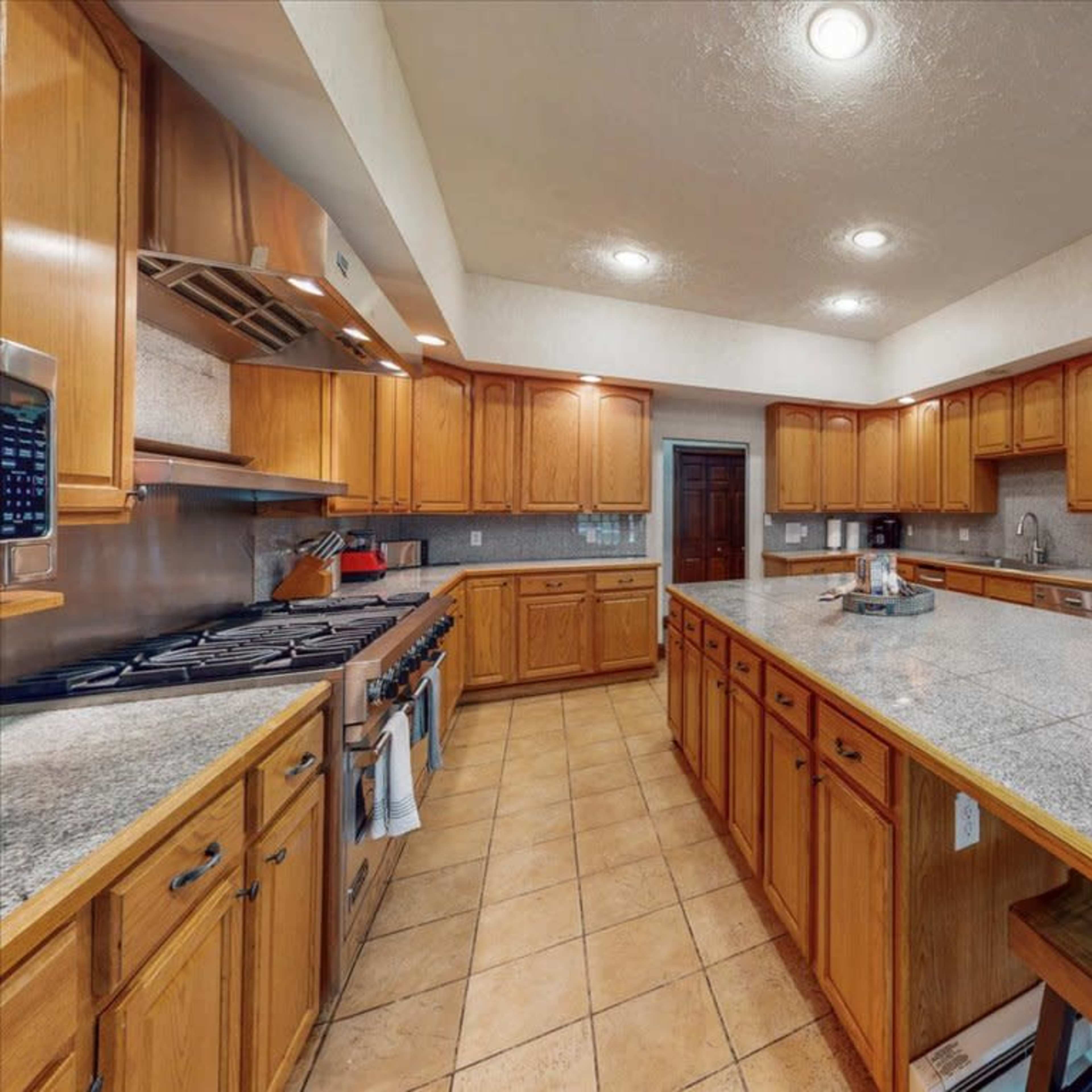 A spacious kitchen with wooden cabinets, a central island, and tiled flooring.
