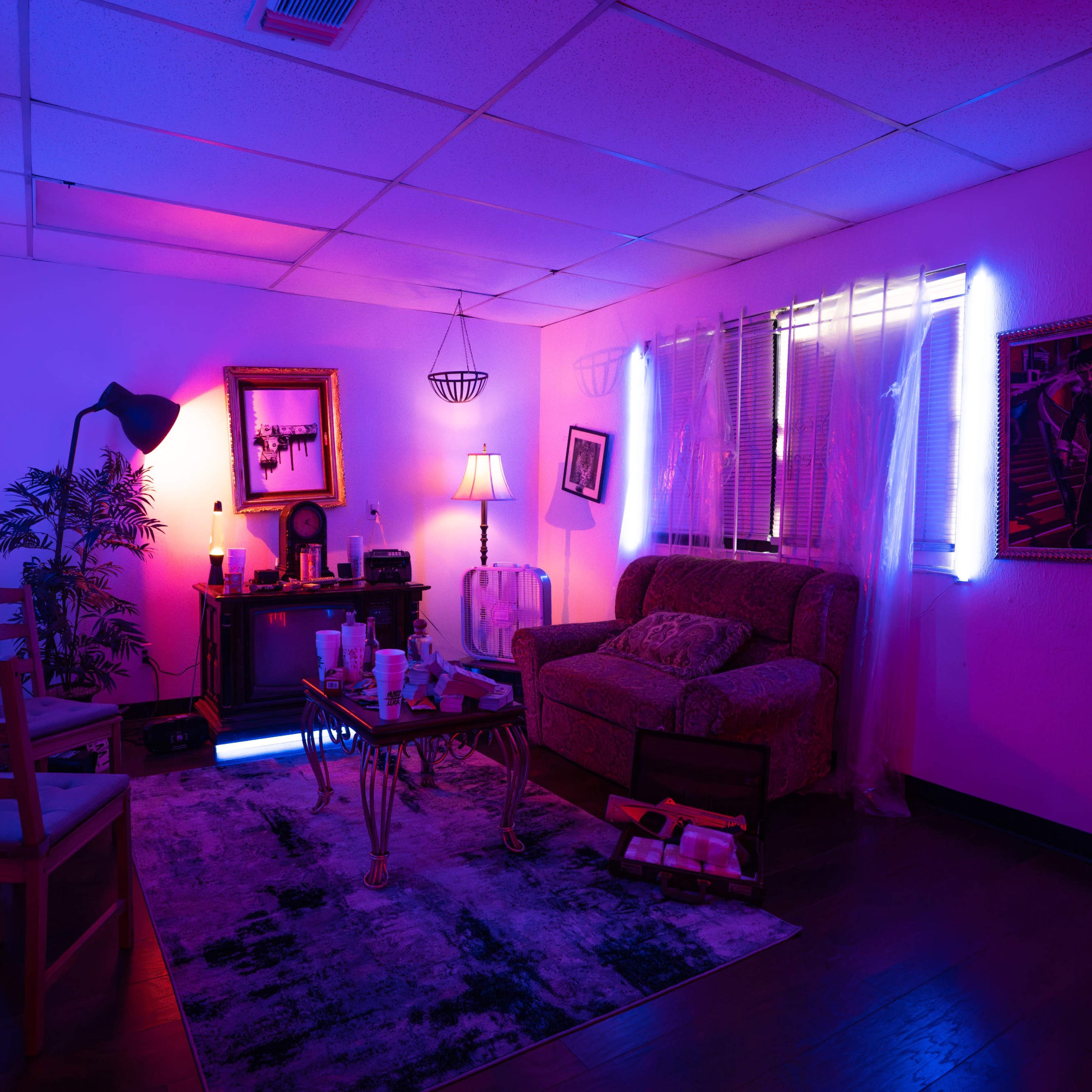A dimly lit room with purple and blue lighting, featuring a couch, chairs, a coffee table, and decorative artwork on the walls.